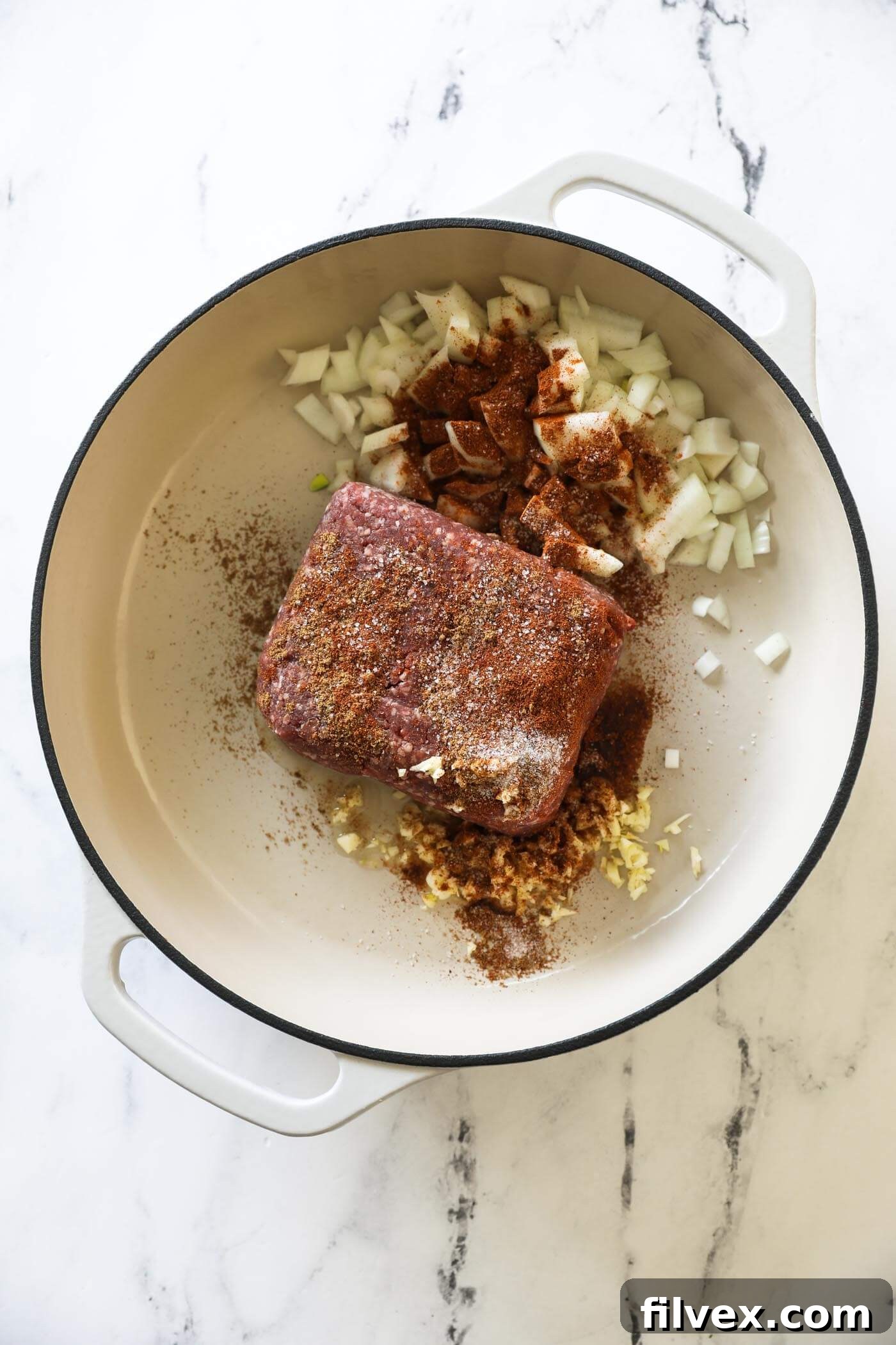 Ground beef, diced onion, minced garlic, and a medley of seasonings (chili powder, cumin, and salt) being added to a hot skillet, ready to be browned.