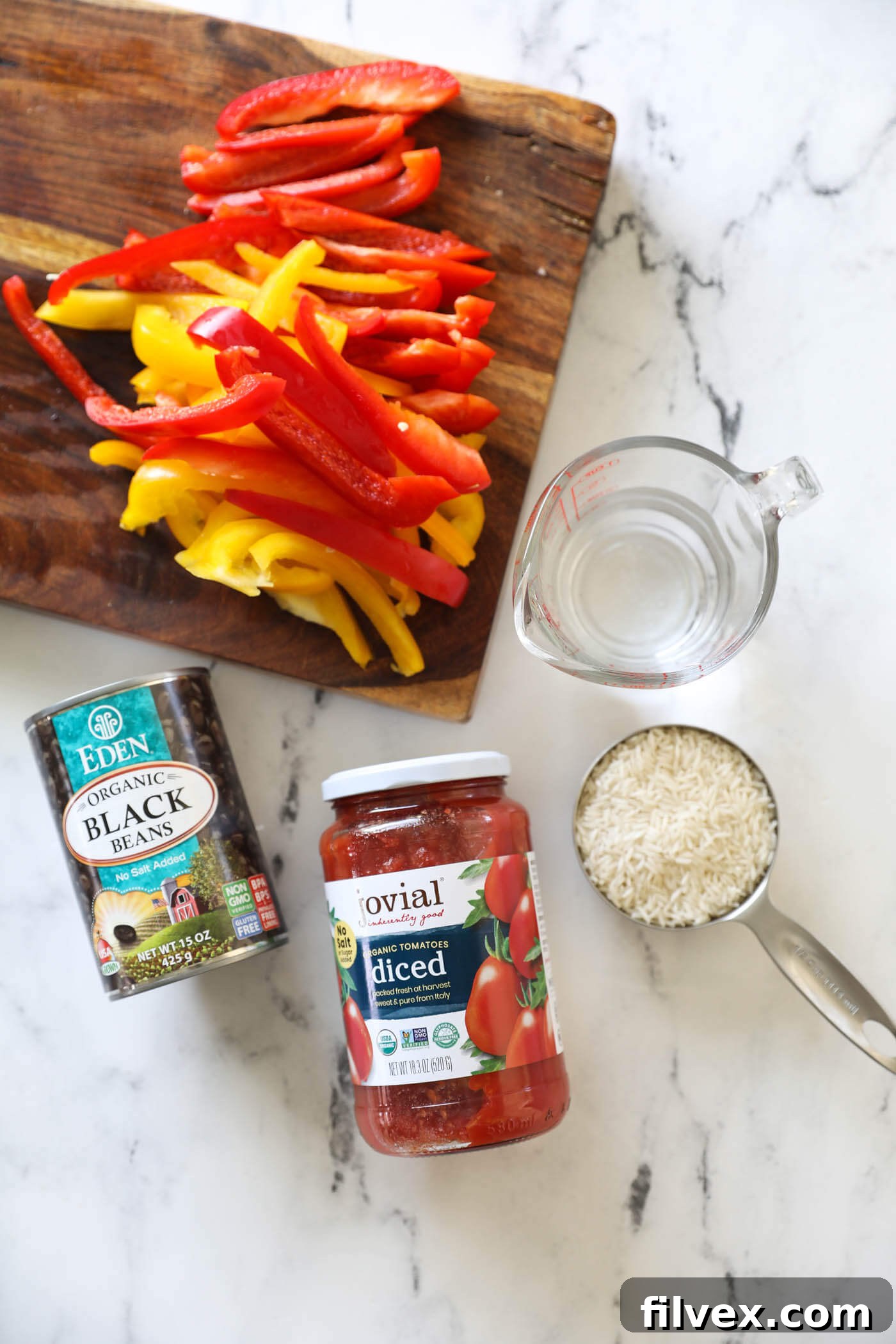 Assorted ingredients including a can of diced tomatoes, a measuring cup of uncooked white rice, and a glass of water, all neatly organized on a kitchen counter.