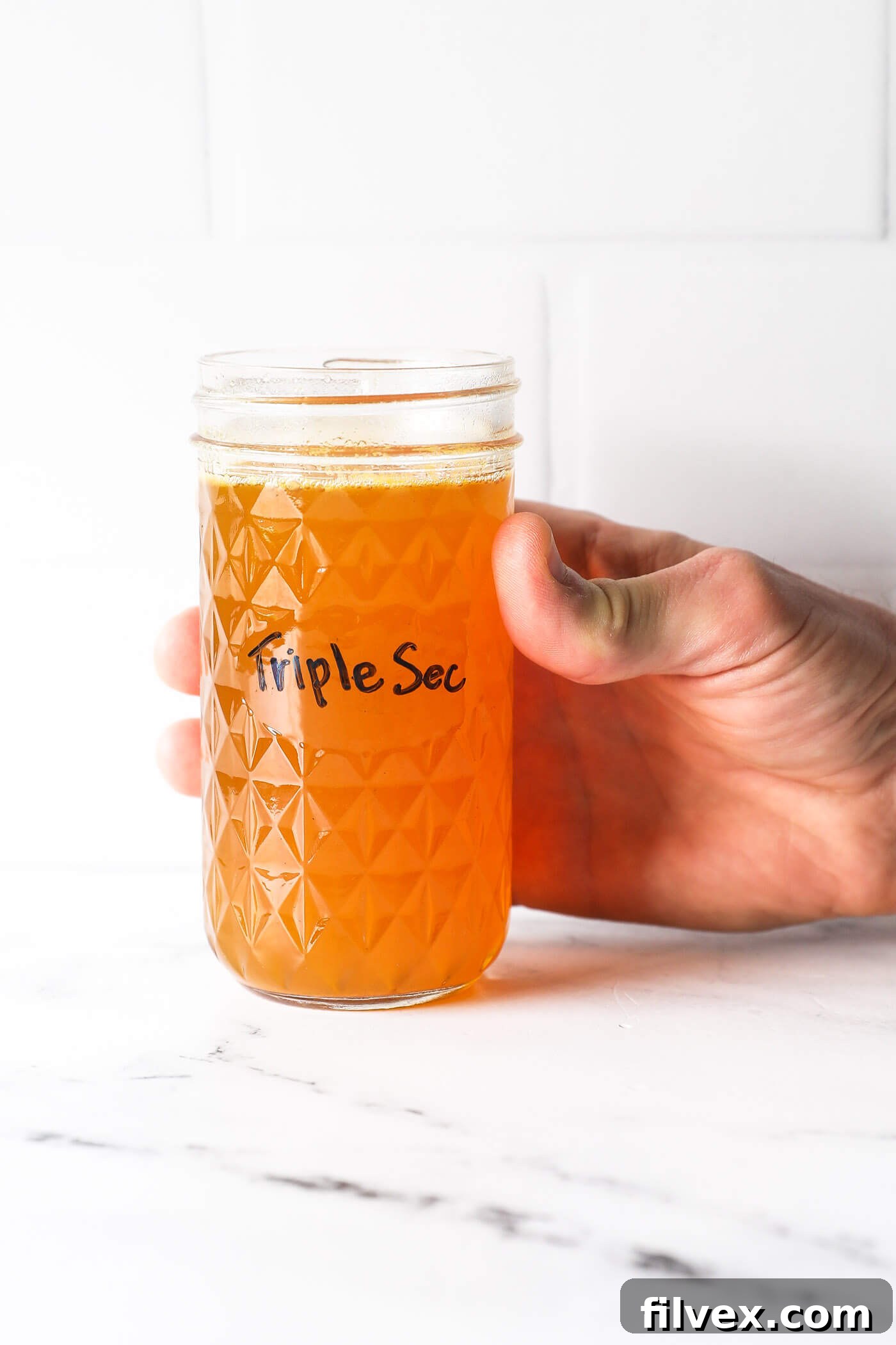 A jar of homemade non-alcoholic triple sec with fresh oranges and a spoon