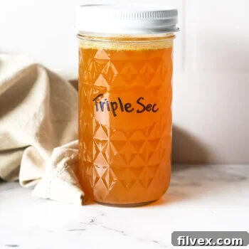 A jar of homemade triple sec with a white cap, glowing with orange color