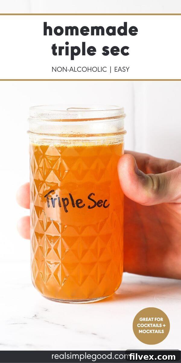 A beautiful jar of homemade non-alcoholic triple sec, glowing with orange hues, held by a hand
