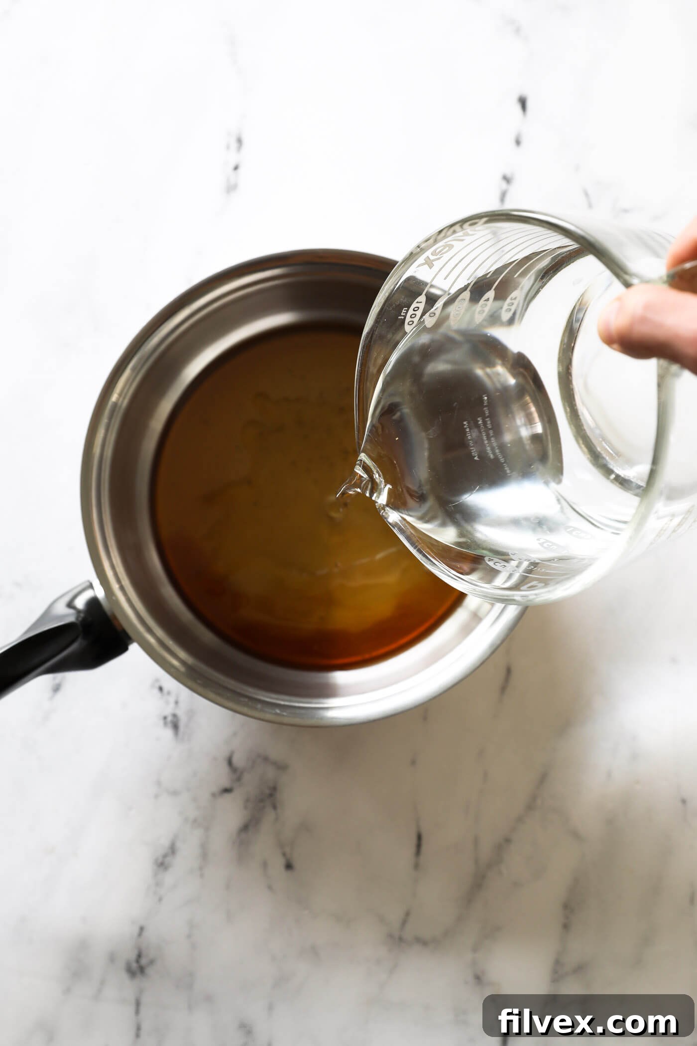 Honey, maple syrup, and water being added to a saucepan on a stove