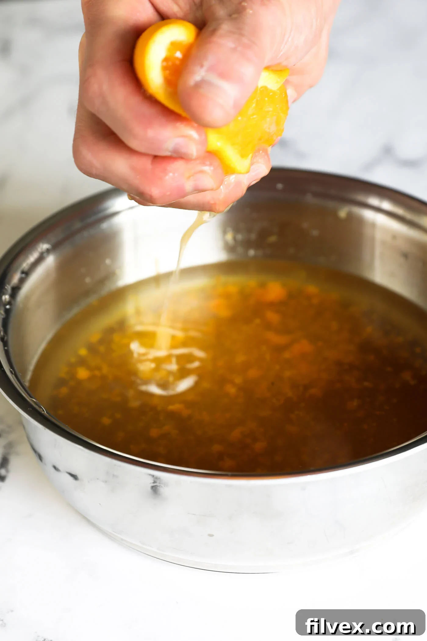 Fresh orange juice being squeezed into the saucepan with the syrup and zest