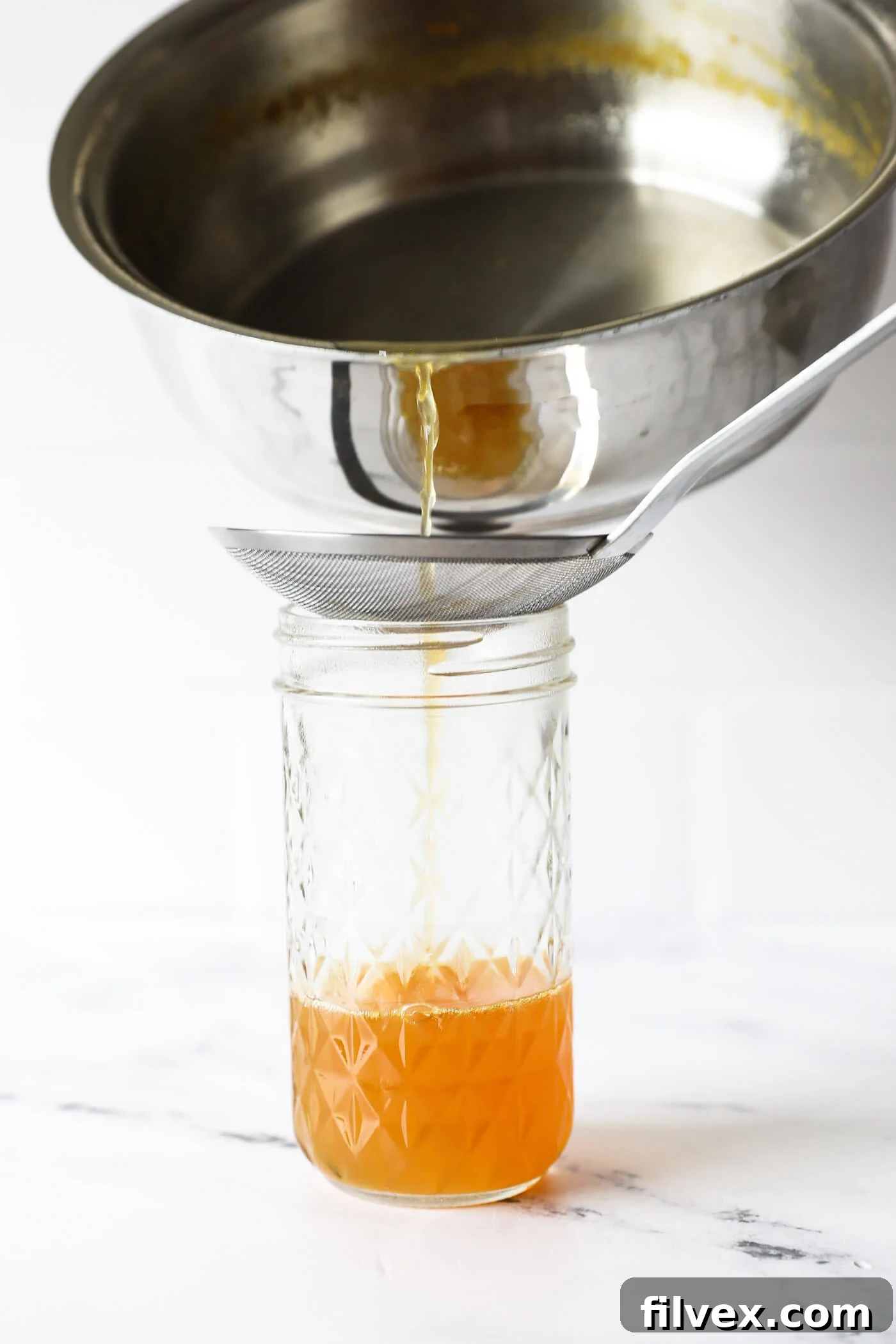 Straining the homemade non-alcoholic triple sec through a fine mesh strainer to remove zest and pulp