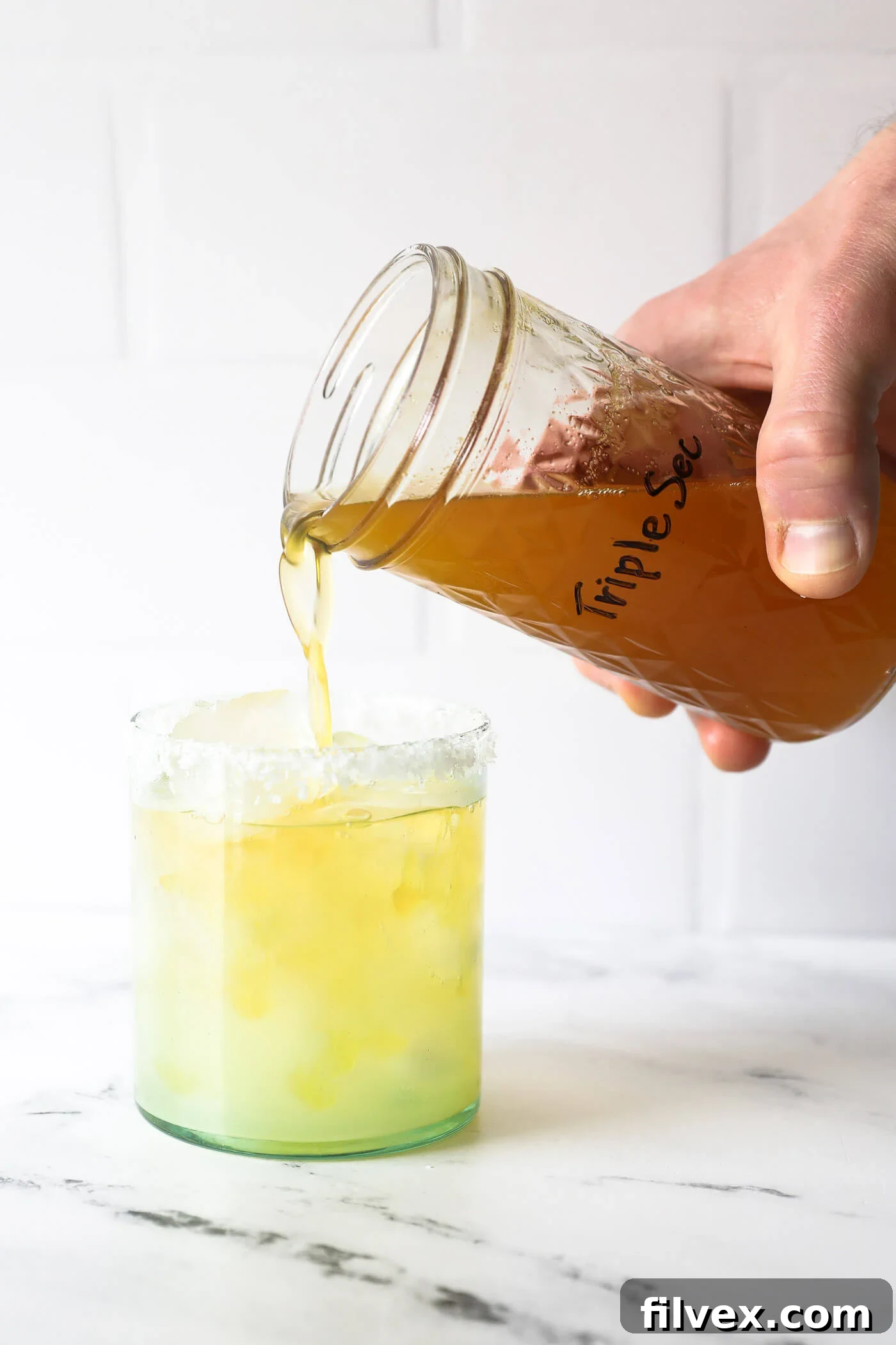 A hand holding a jar of homemade non-alcoholic triple sec, ready to be used in a virgin margarita