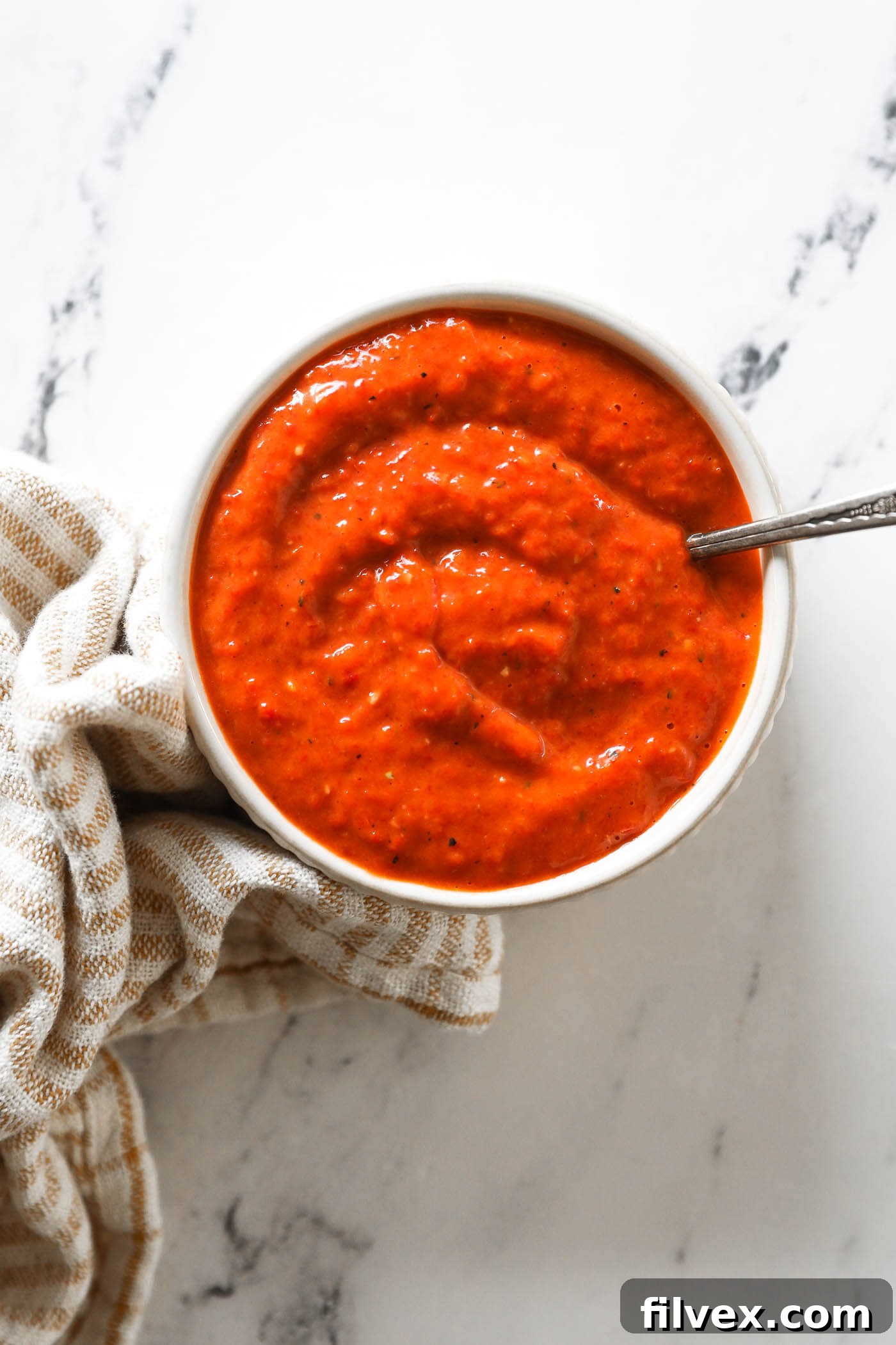 A beautiful, vibrant red pepper sauce displayed in a white bowl, ready to be served as a dip or topping.