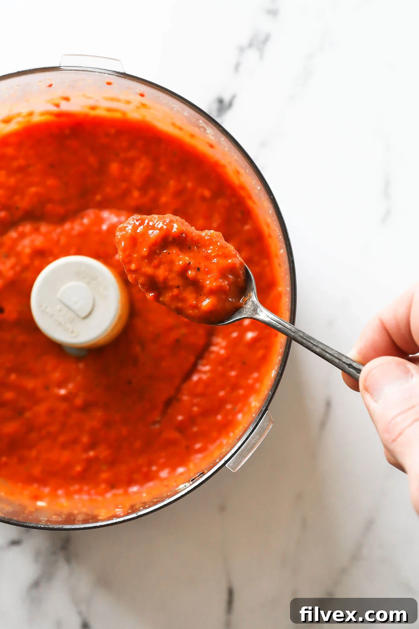 The red pepper sauce being processed in a food processor, achieving a smooth and creamy texture, with the blades visibly active.