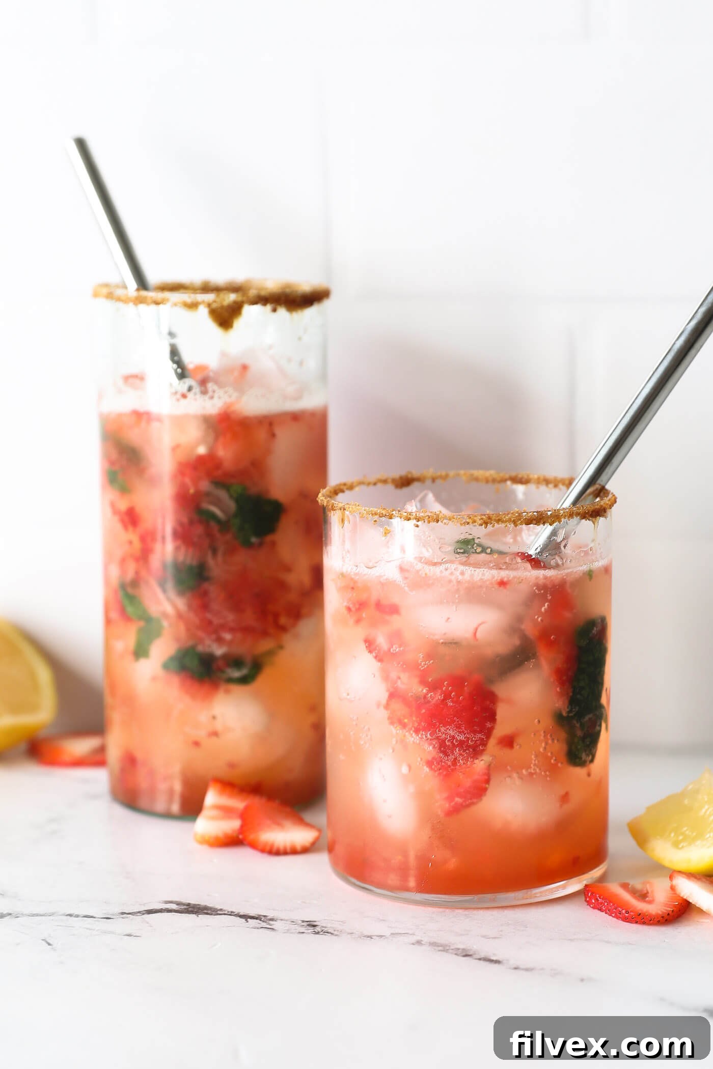 A tall, elegant glass filled with a vibrant red strawberry basil mocktail, garnished with fresh basil leaves and a slice of lemon. The drink contains muddled strawberries and ice, reflecting a bright, airy setting.