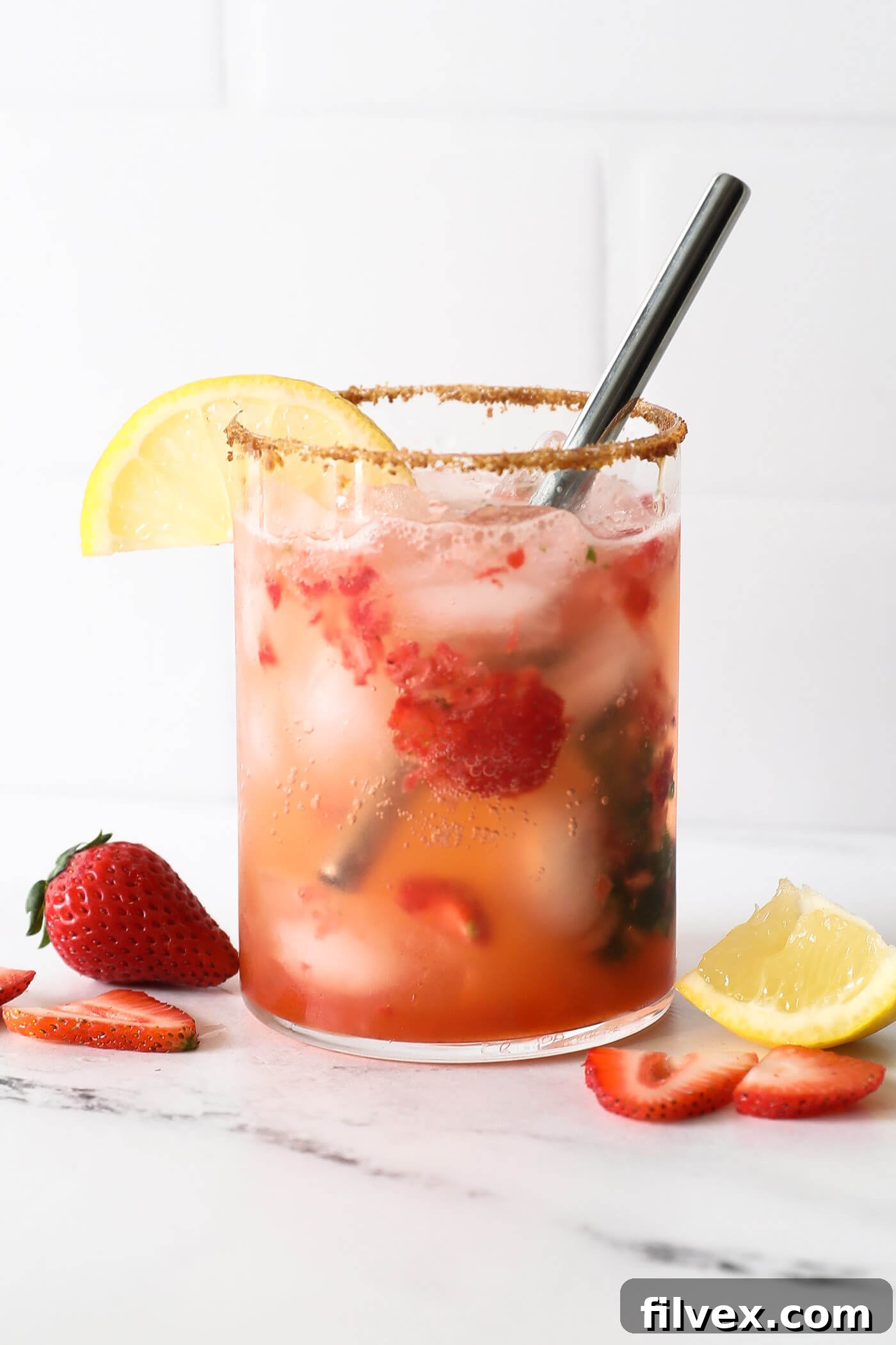 A close-up shot of a refreshing Strawberry Basil Mocktail in a clear glass, showing the muddled strawberries and basil, ice cubes, and a vibrant lemon slice garnish. The texture of the fruit is visible.