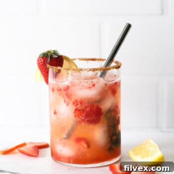 Straight on shot of vibrant red strawberry basil mocktail with a strawberry and lemon wedge garnish in a tall glass, against a soft background.