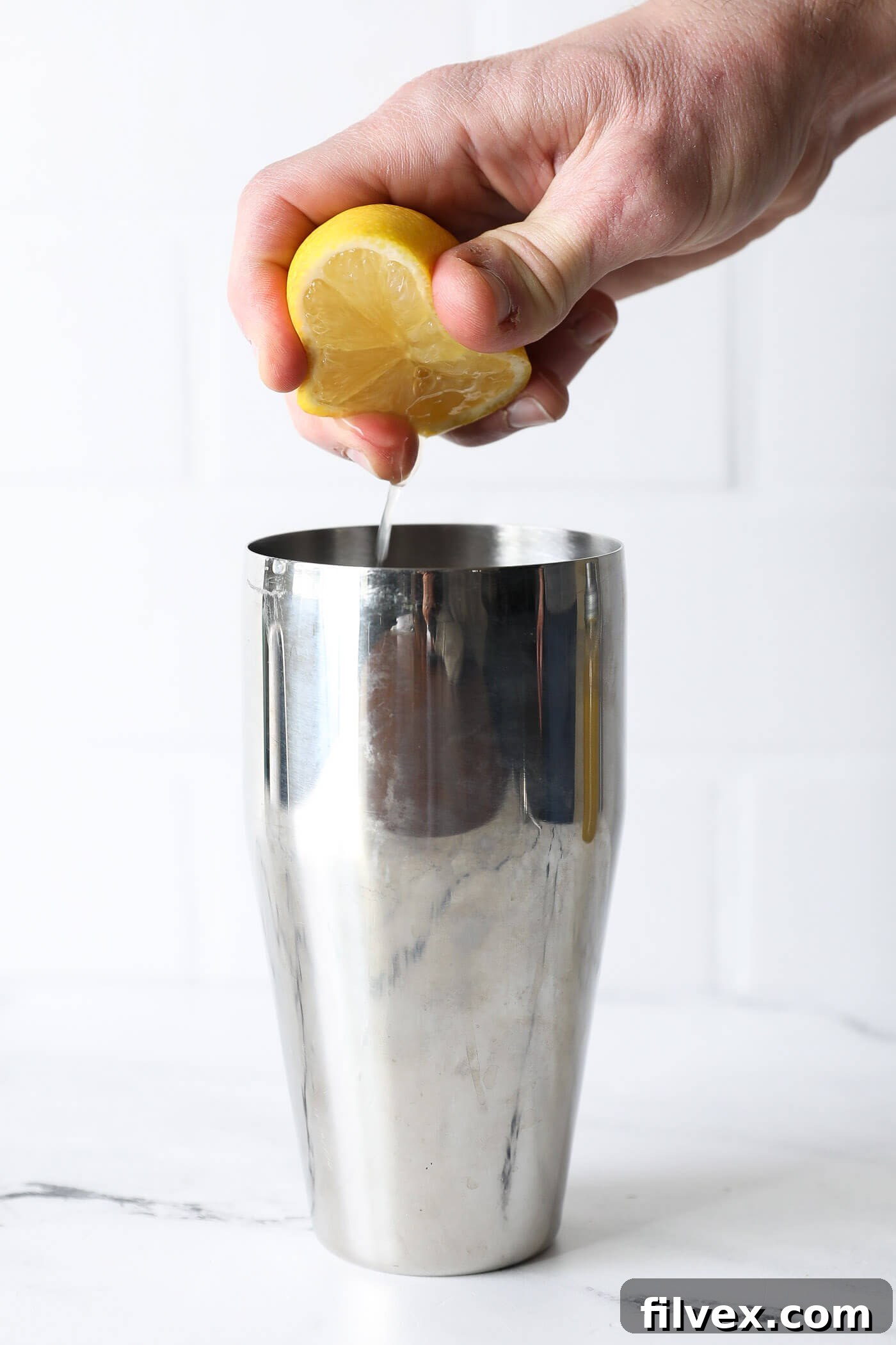 Freshly squeezed lemon juice is being added to the mixture in the cocktail shaker, completing the liquid ingredients before shaking.