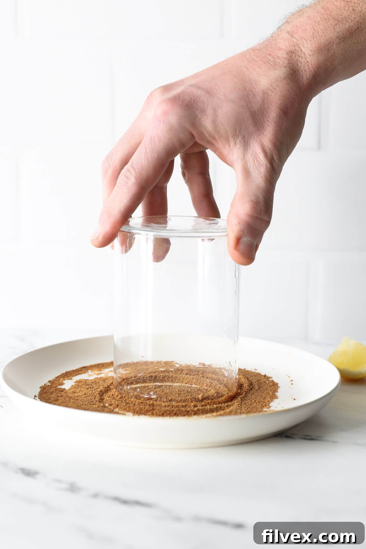 The rim of a glass is dipped into a plate filled with golden coconut sugar, ensuring an even and attractive coating for a sweet finish.