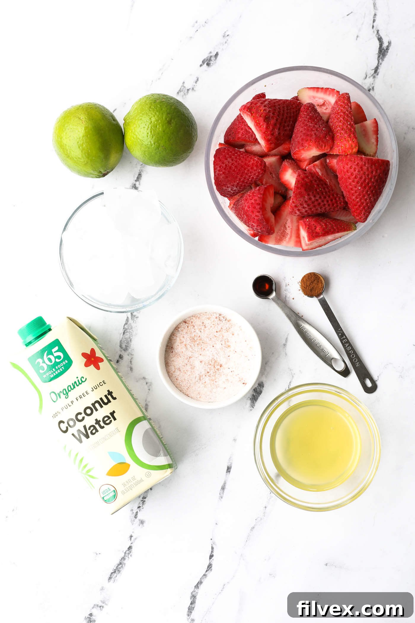 All ingredients for a strawberry daiquiri mocktail laid out: frozen strawberries, coconut water, lime, syrup, vanilla, cinnamon, salt, and ice.