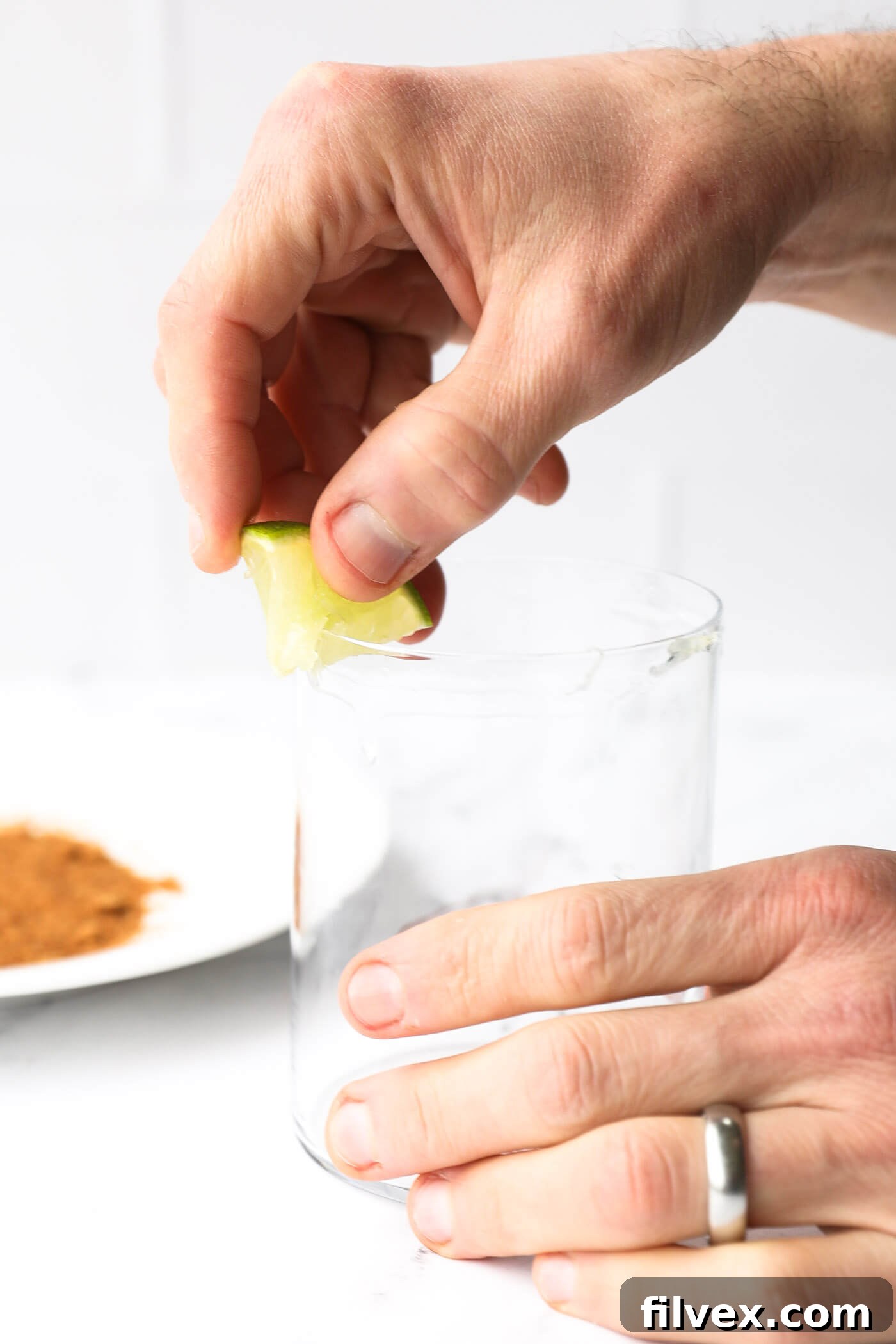 A lime wedge being run around the rim of a glass, preparing it for a sugar coating.