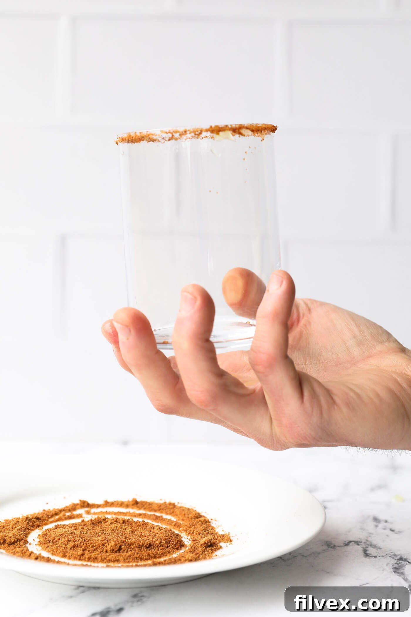 The rim of a glass being dipped into a plate of coconut sugar, creating a beautiful sugary edge.