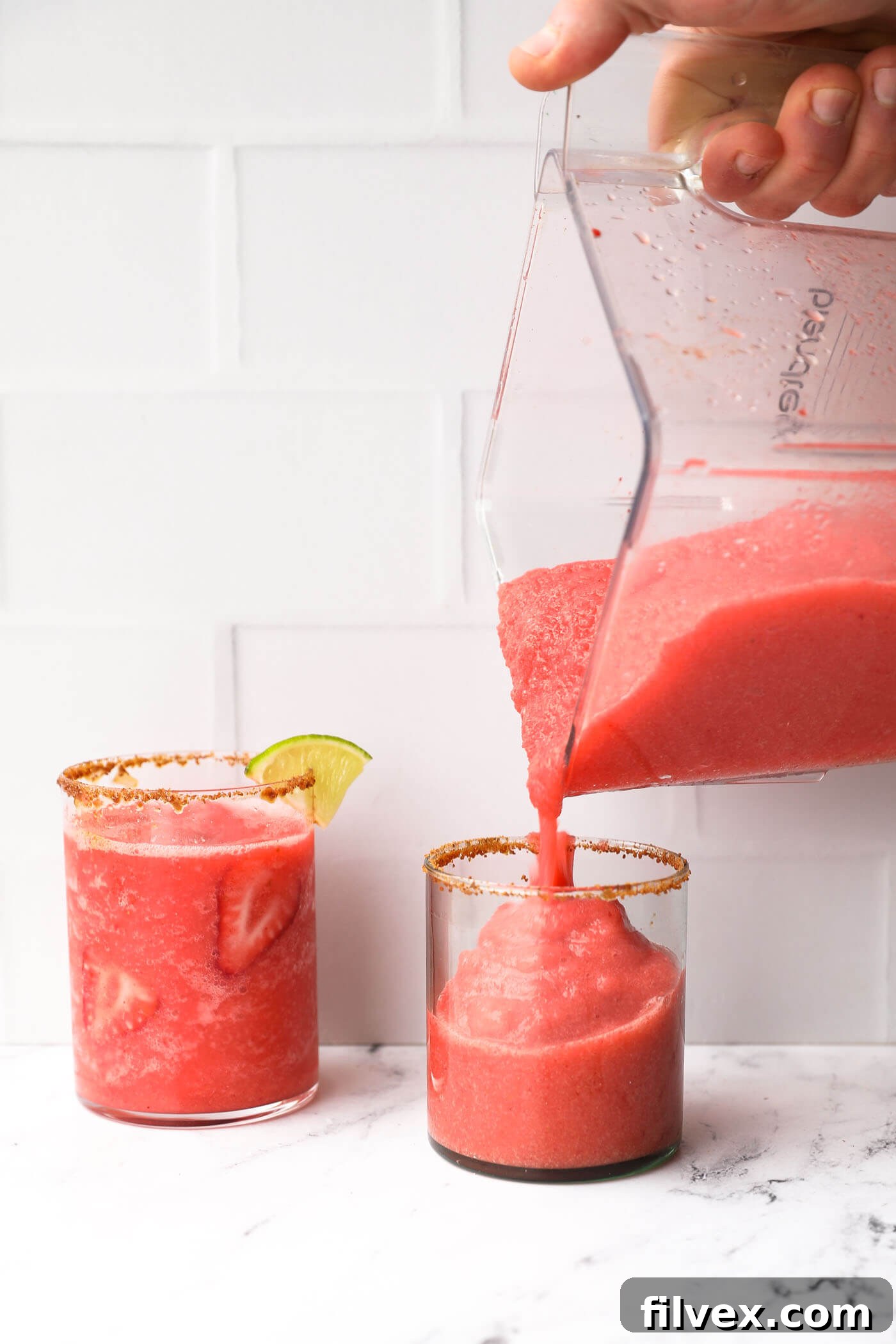 A freshly blended strawberry daiquiri mocktail being poured into a sugar-rimmed glass, ready for serving.
