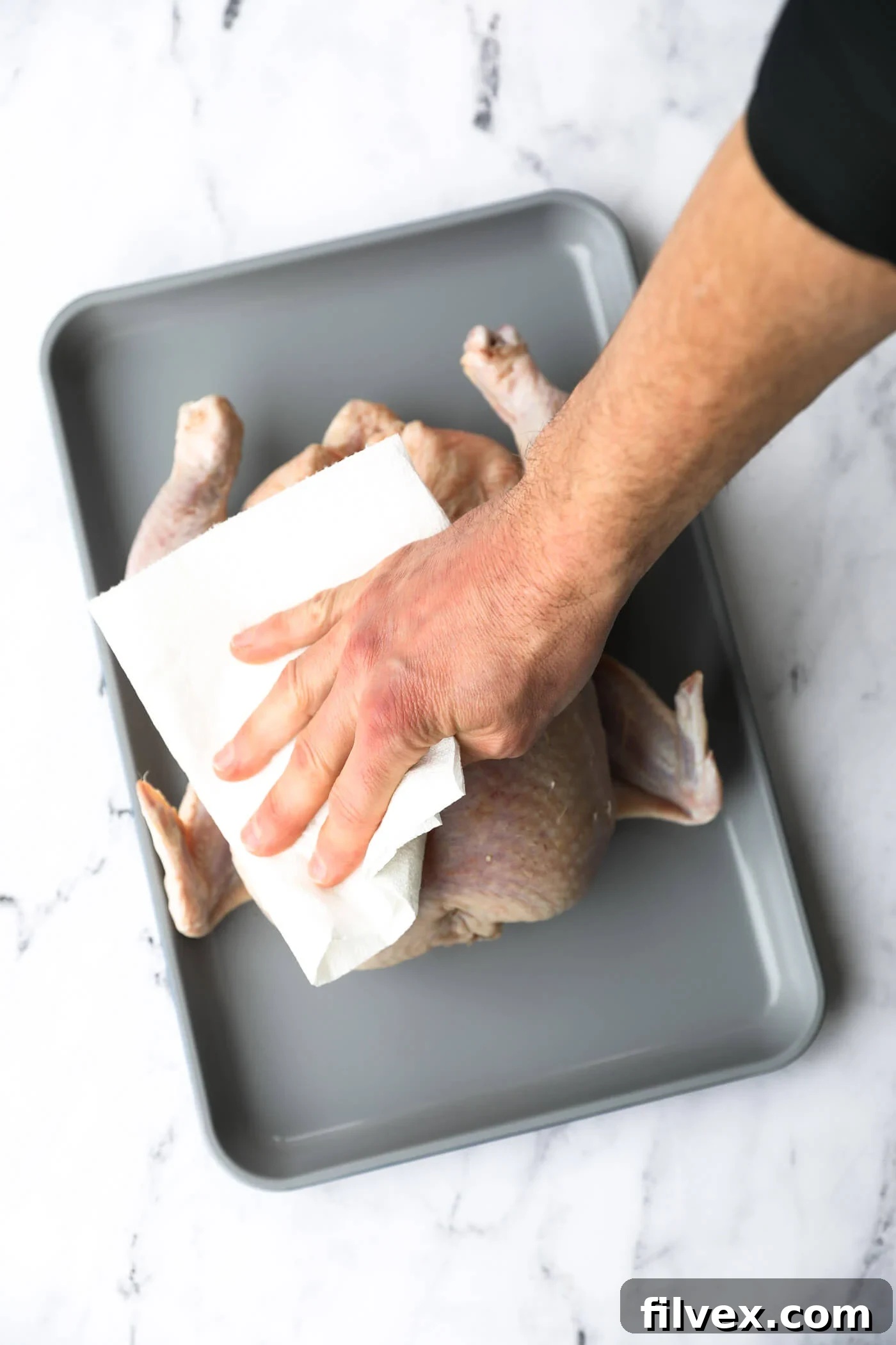 Patting a whole chicken dry with paper towels to prepare for seasoning.