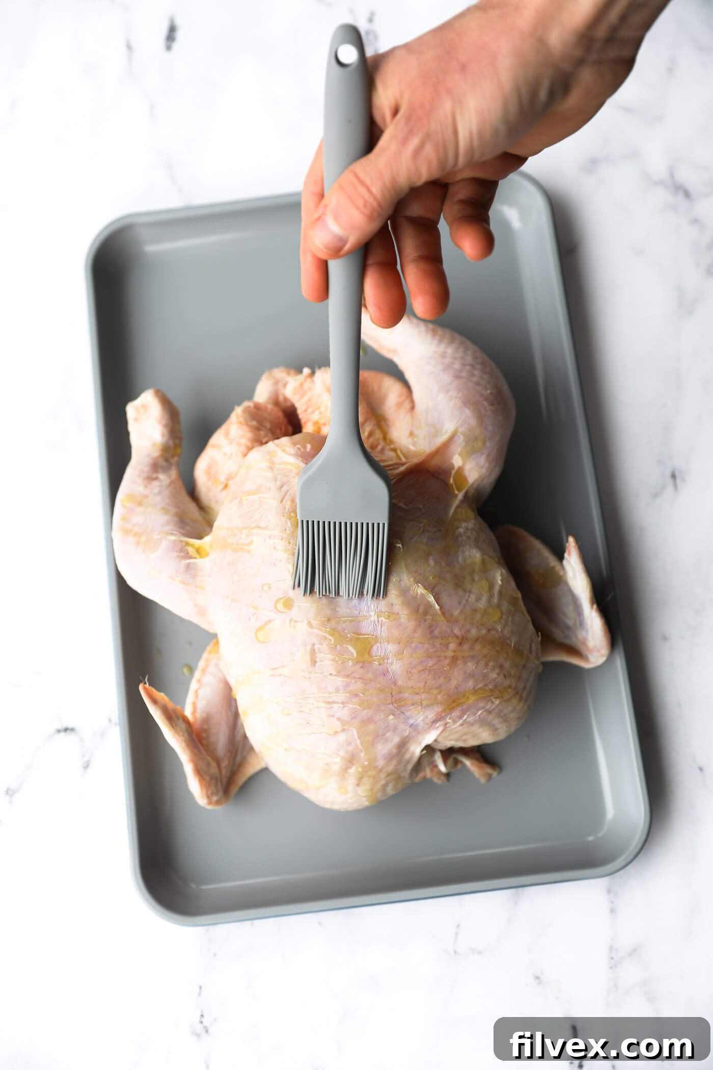 Drizzling olive oil over a whole chicken and brushing it to coat evenly.