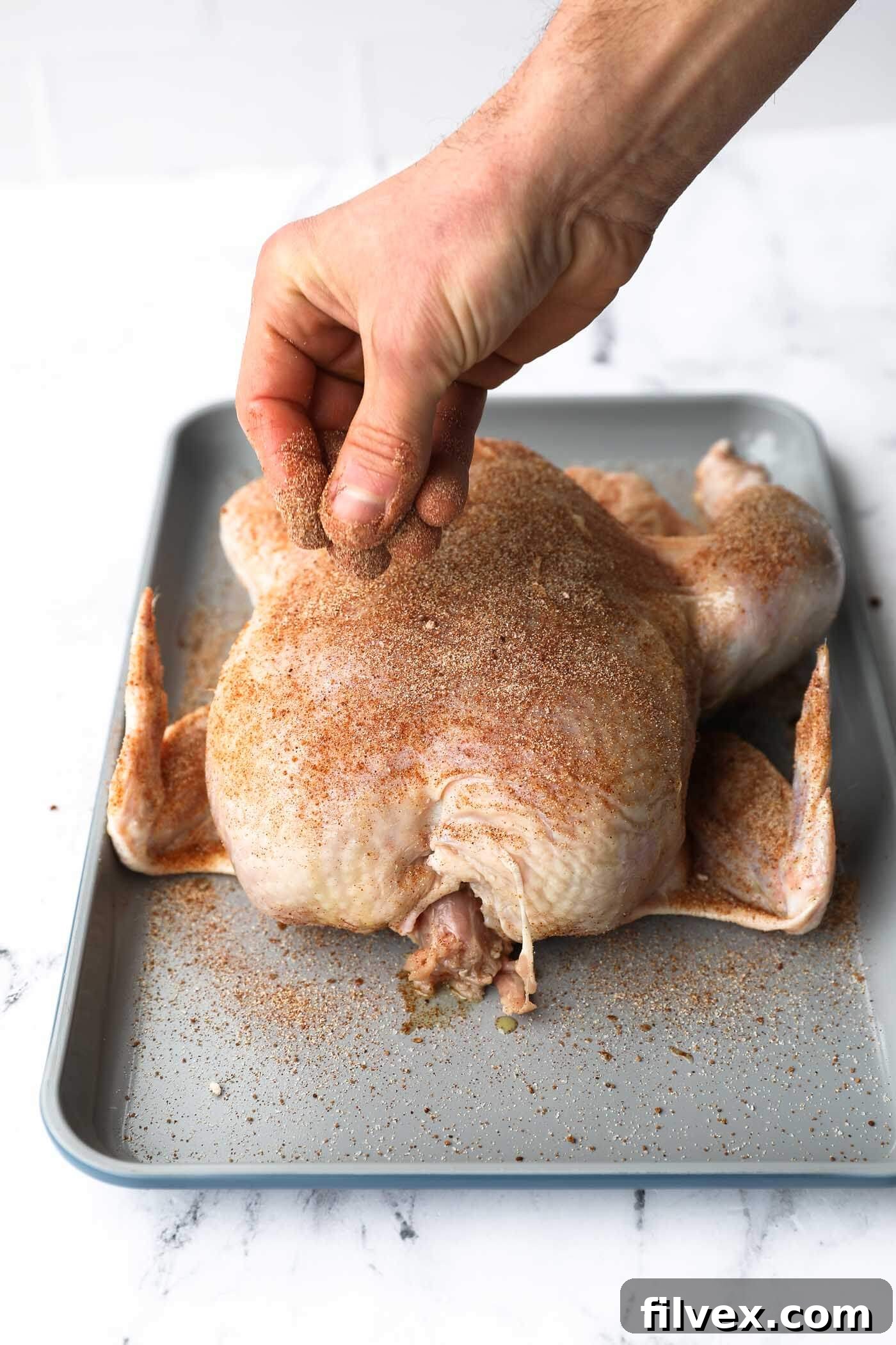 Seasoning a whole chicken liberally with the prepared rub.