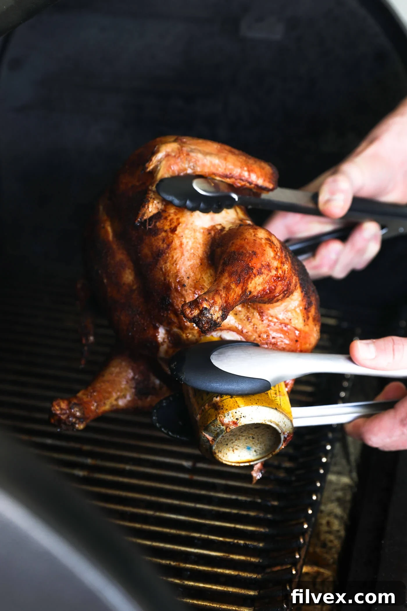 Safely removing the hot beer can from the chicken cavity using two sets of tongs.