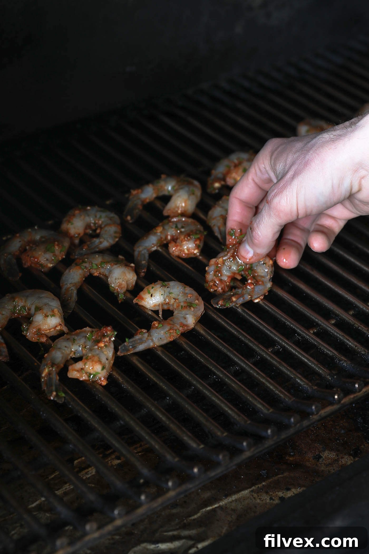 Marinated shrimp artfully arranged directly on the hot grill grates of a smoker, with a visible smoky haze, as they begin to cook and transform into a luscious pink hue.