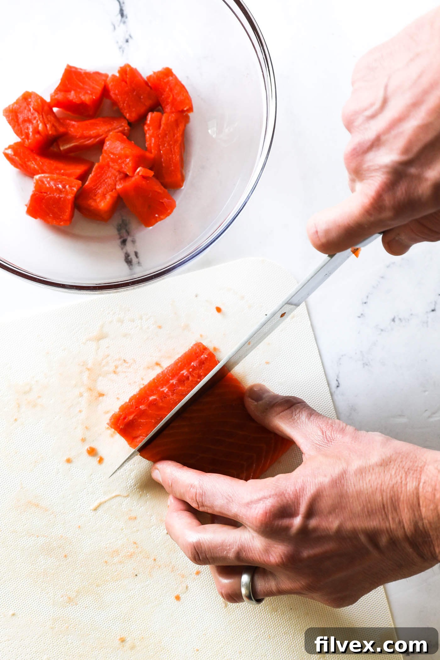 Cutting raw salmon fillets into even 1-inch bite-sized cubes