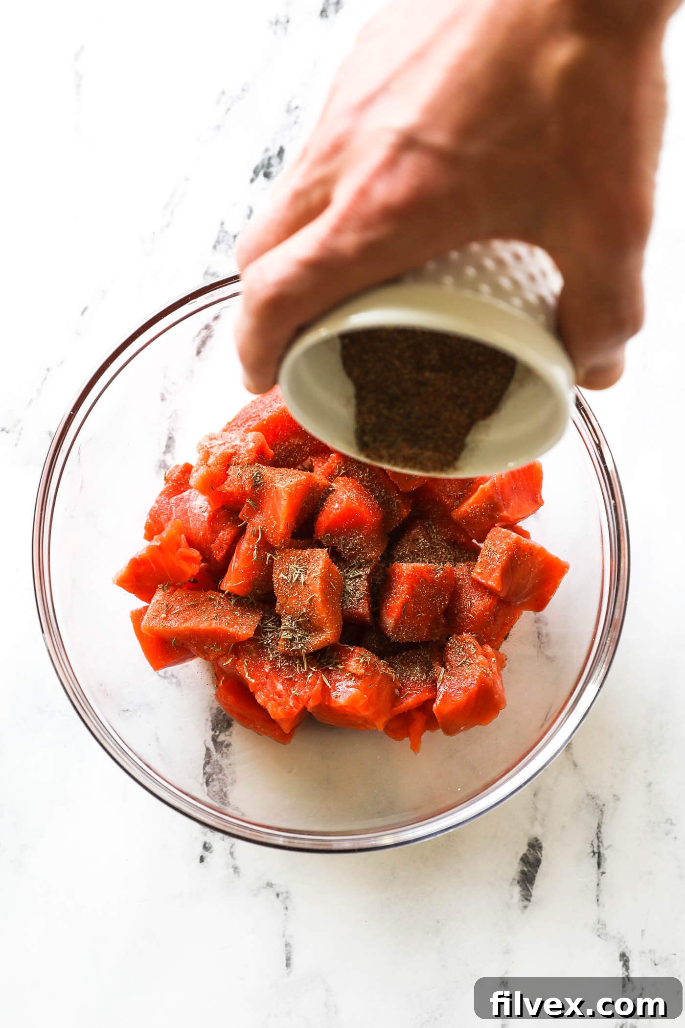 Sprinkling generous amount of seasoning over salmon cubes in a bowl