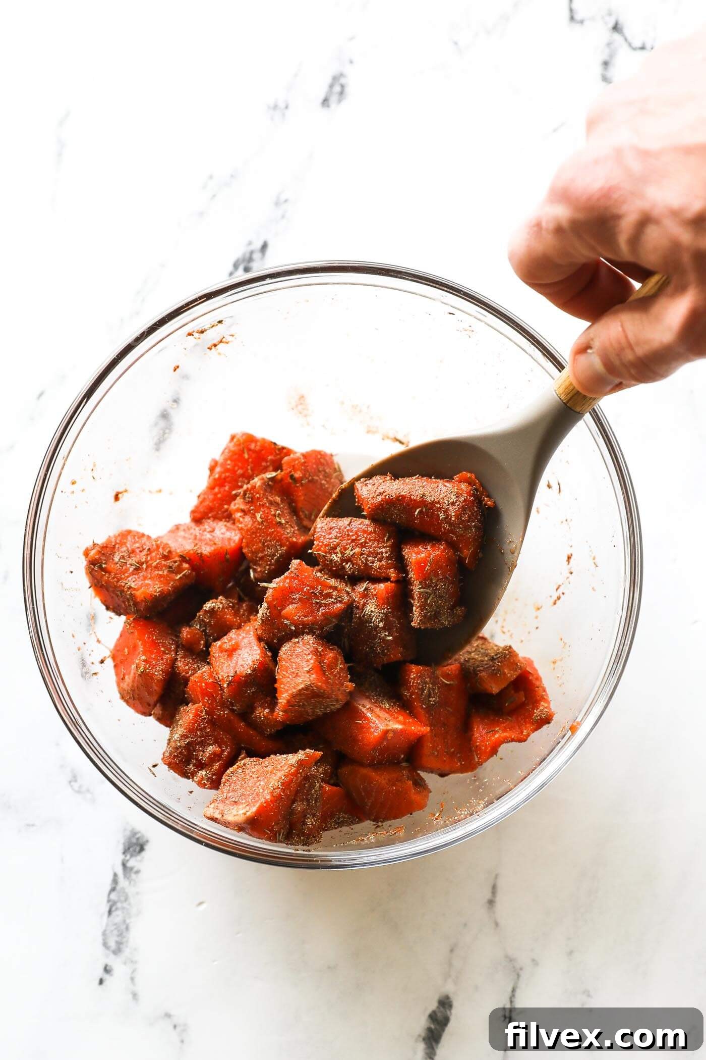 Tossing salmon cubes by hand to evenly coat with seasoning