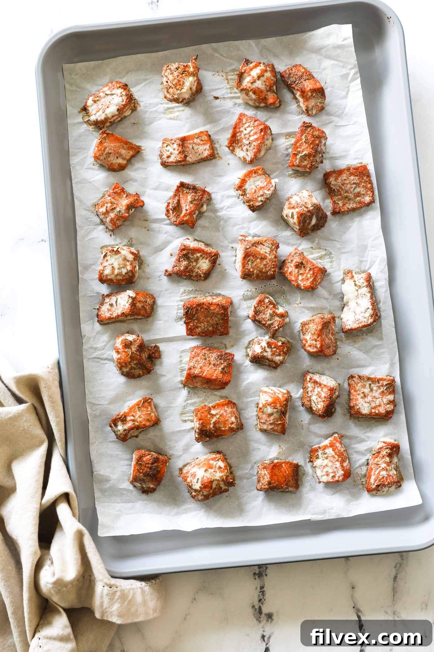 Golden brown cooked salmon bites on parchment paper lined baking sheet, garnished with fresh herbs