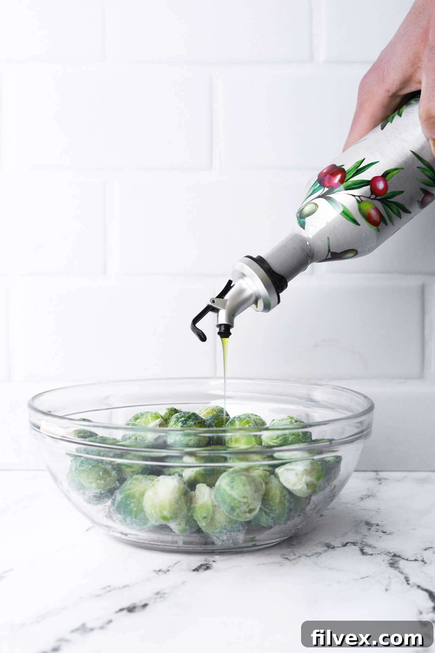 Drizzling olive oil over frozen Brussels sprouts in a bowl.