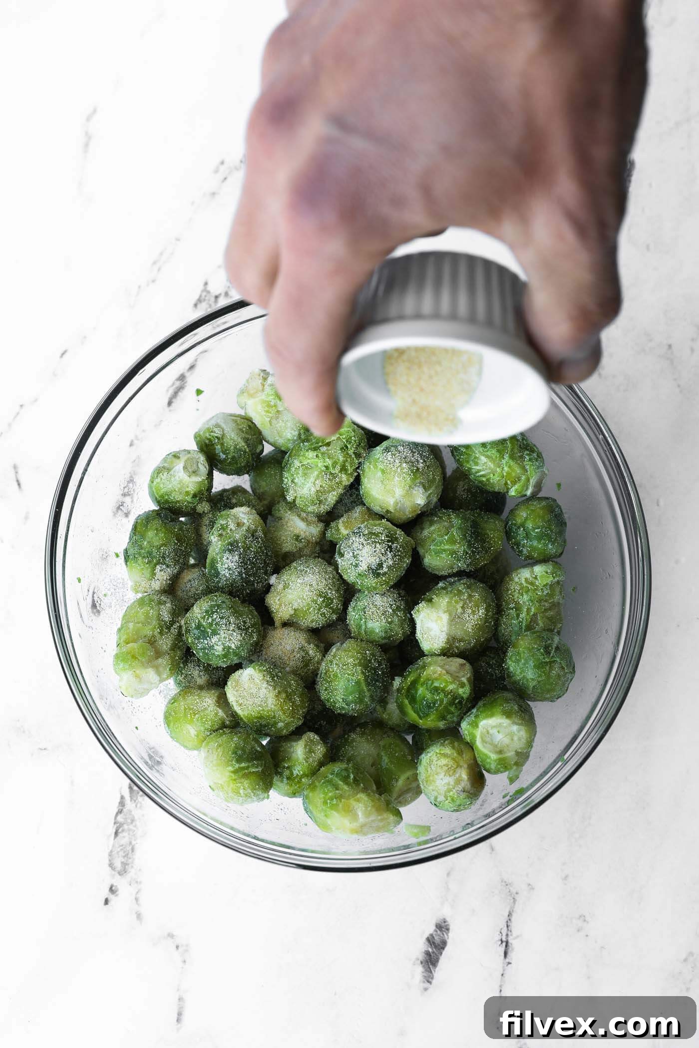 Adding the prepared seasoning mix over olive oil-coated frozen Brussels sprouts.