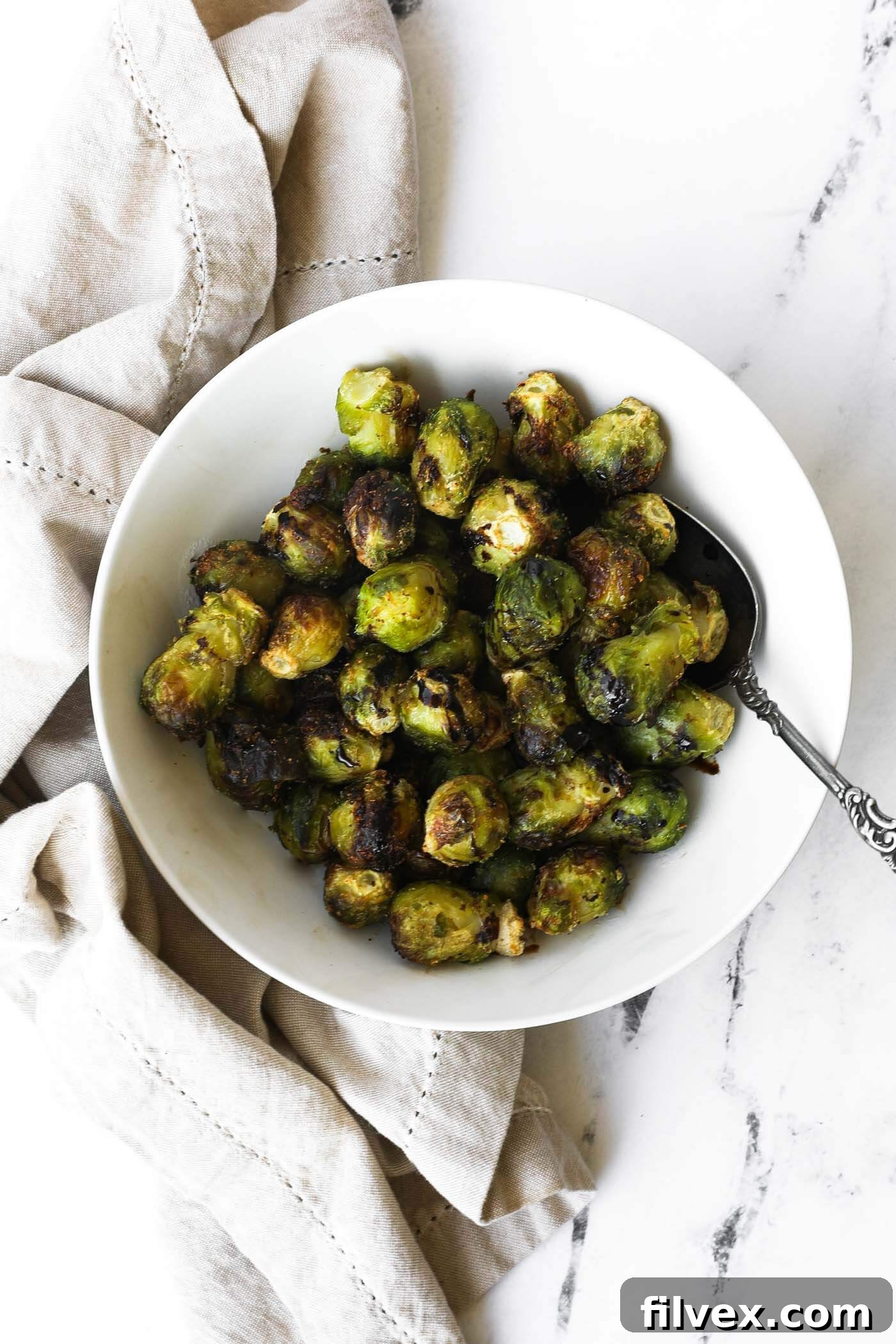A bowl of freshly cooked, golden-brown air fryer frozen Brussels sprouts, topped with a balsamic glaze.
