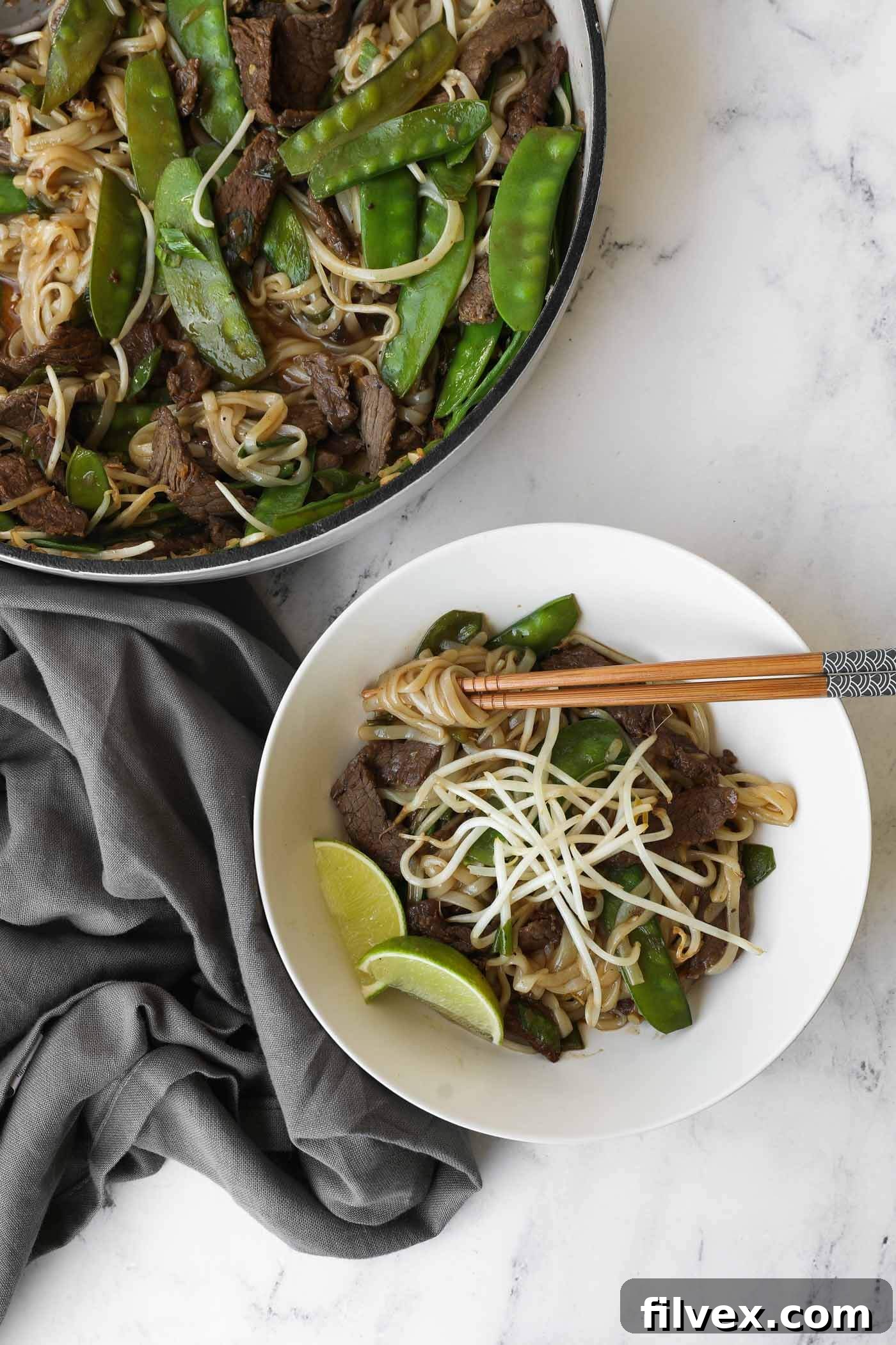 A vibrant, close-up overhead shot of homemade Beef Pad Thai, garnished with fresh lime wedges and red pepper flakes, ready to be served.