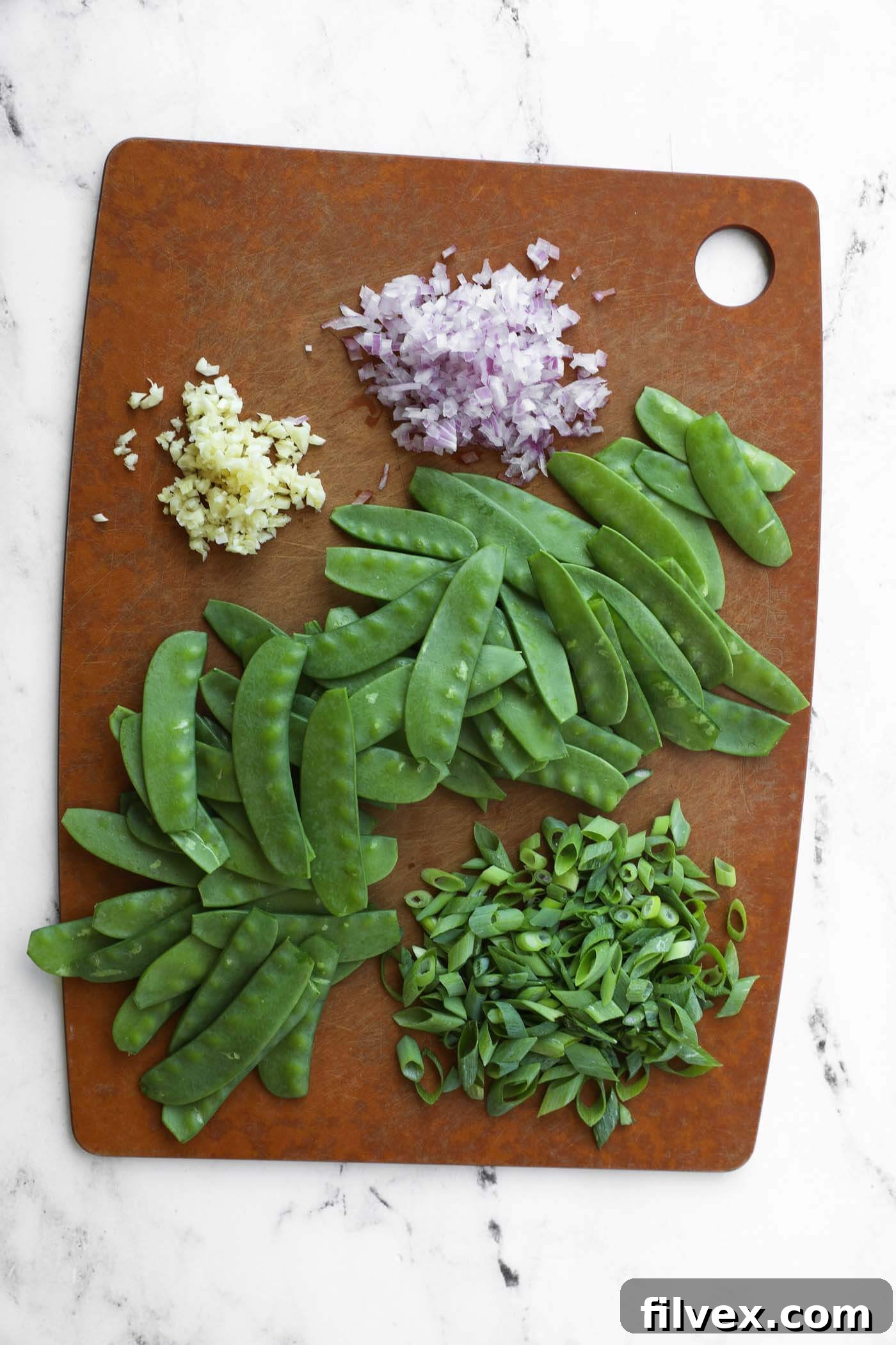 Finely diced shallots, minced garlic, chopped green onions, and trimmed snow peas, meticulously prepped for the stir-fry.