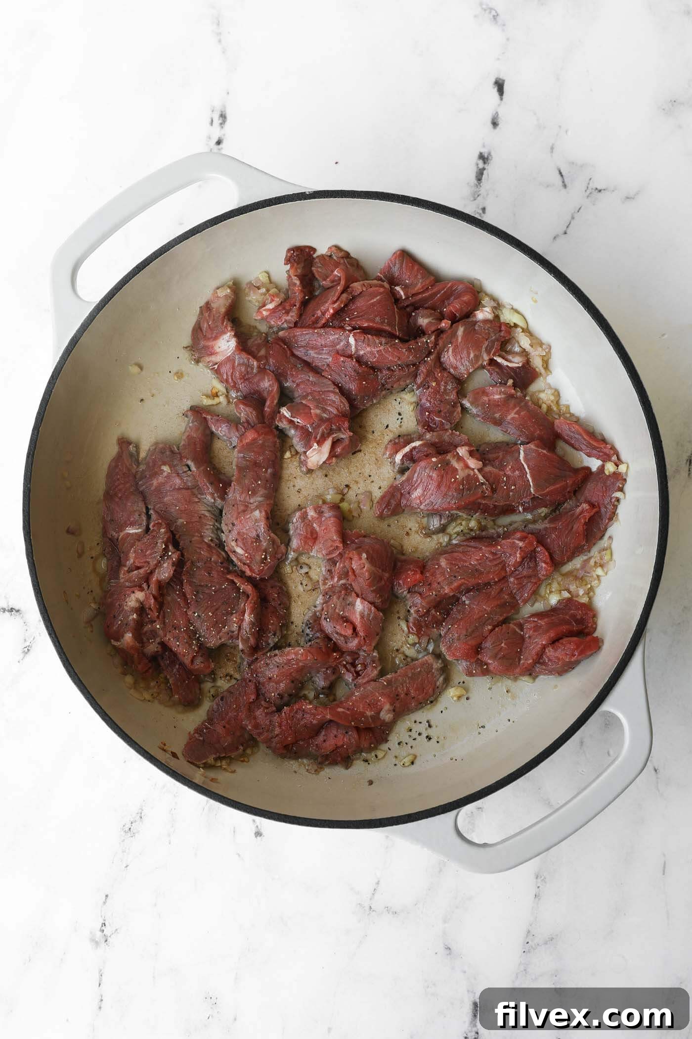 Thinly sliced beef strips are added to the skillet with the aromatics, seasoned with salt and pepper, ready to be seared.