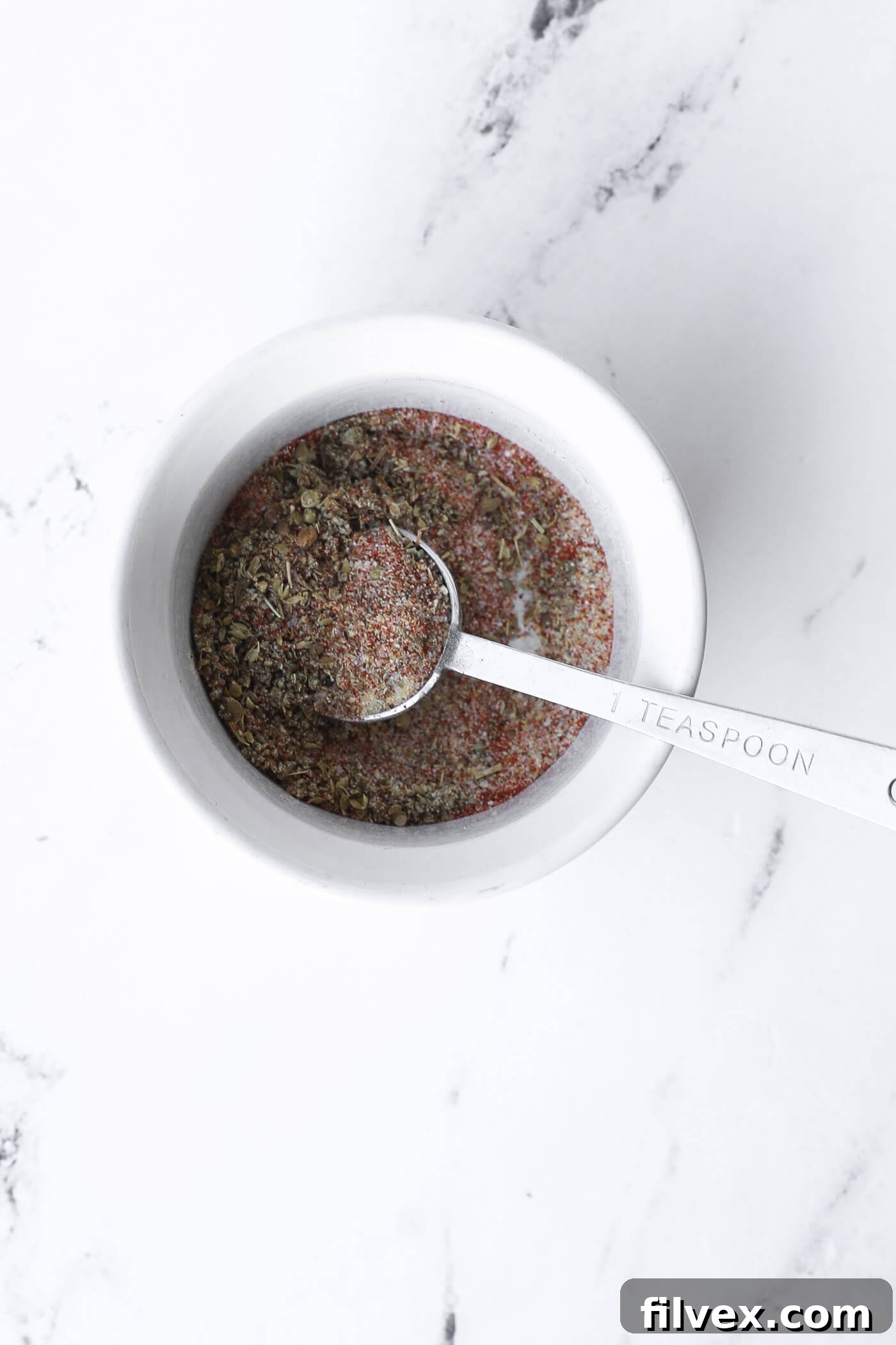 Spices are mixed in a bowl, forming a seasoning blend for the chicken and rice.