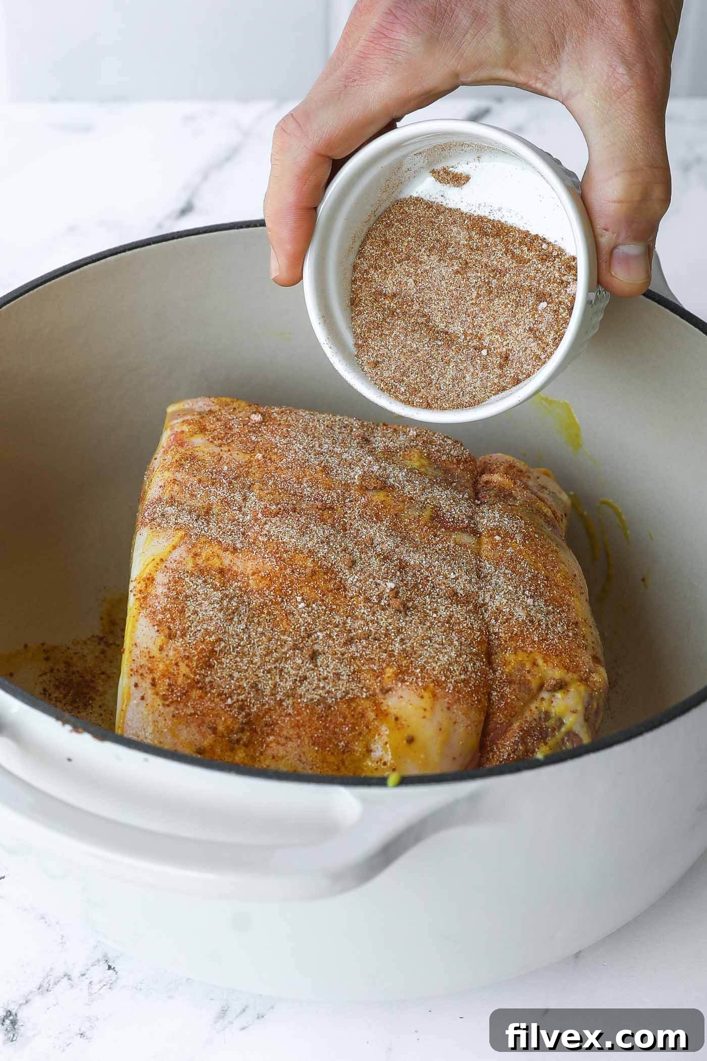 The mustard-coated pork shoulder being generously seasoned with the spice blend.