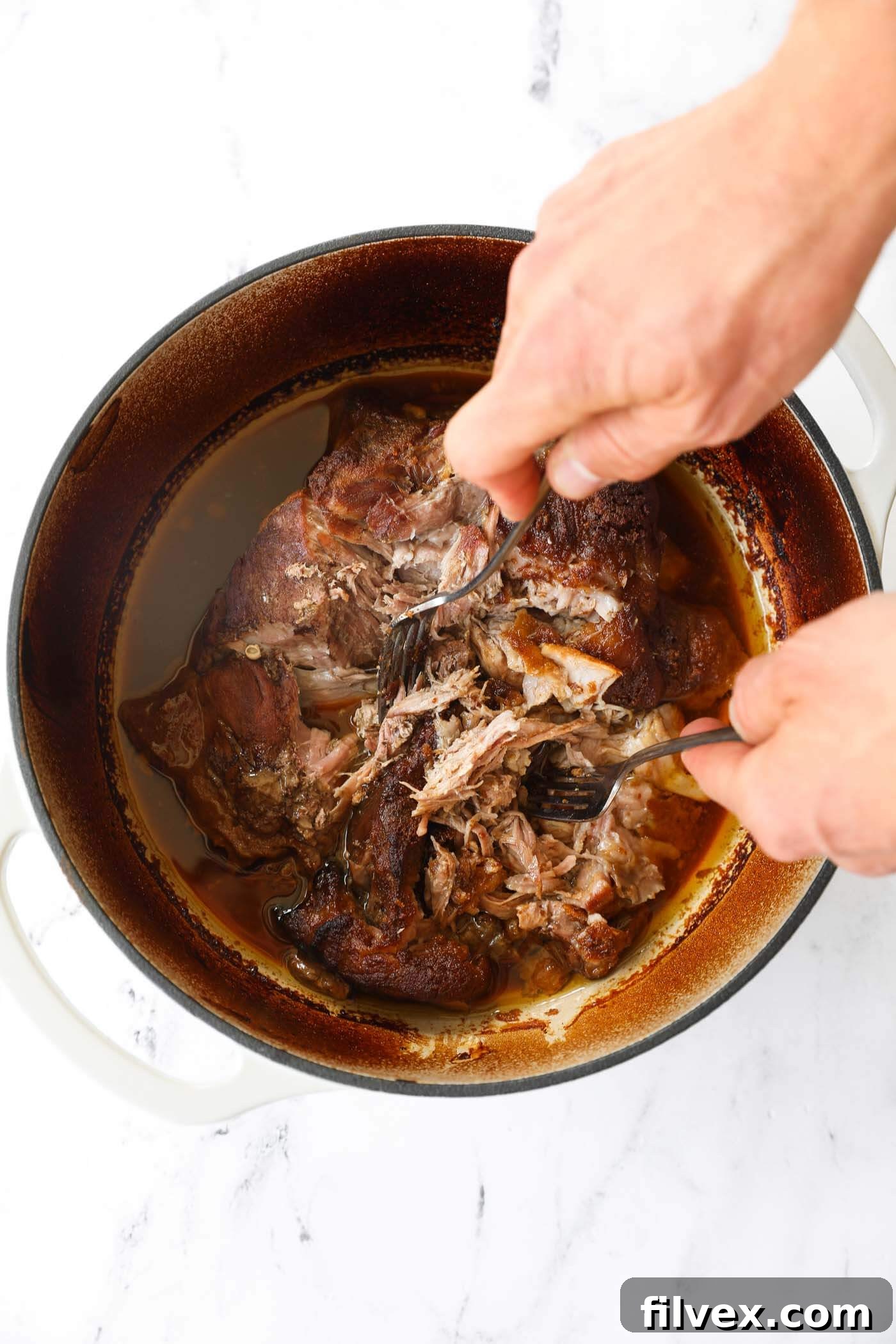 Two forks shredding the tender pulled pork directly in the Dutch oven, mixing it with the savory juices.