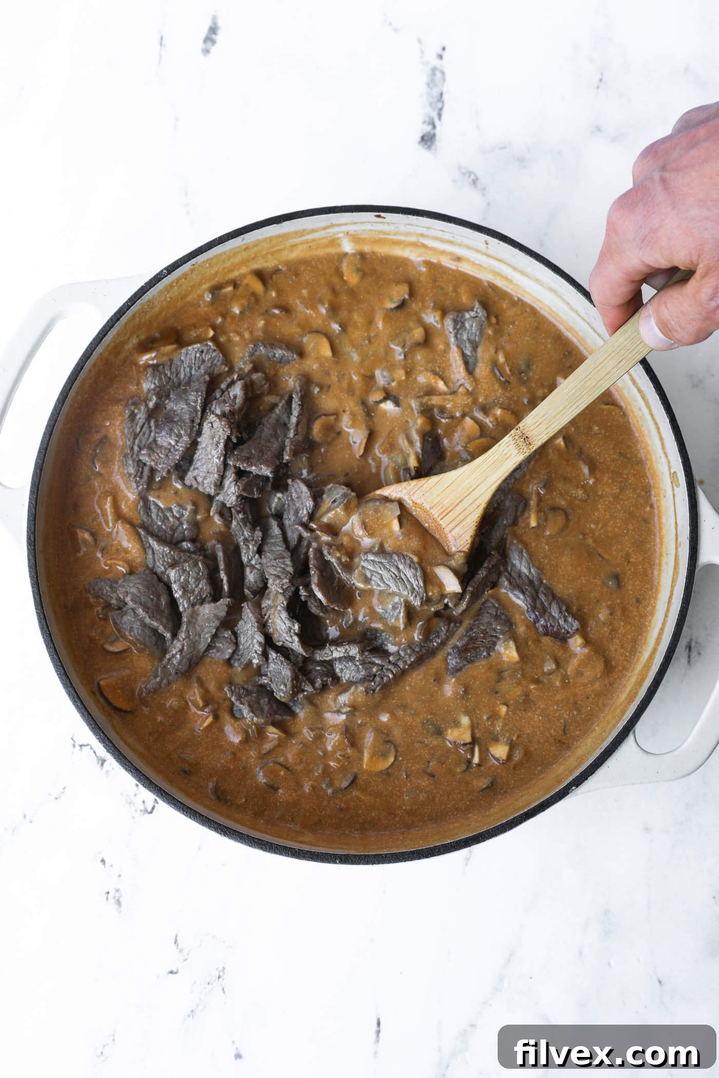 Browned beef strips being returned to the skillet, ready to be tossed with the thick, creamy mushroom sauce.