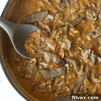 Close up overhead of creamy beef and mushroom skillet with spoon coming out, showcasing the rich texture of the sauce and tender beef.