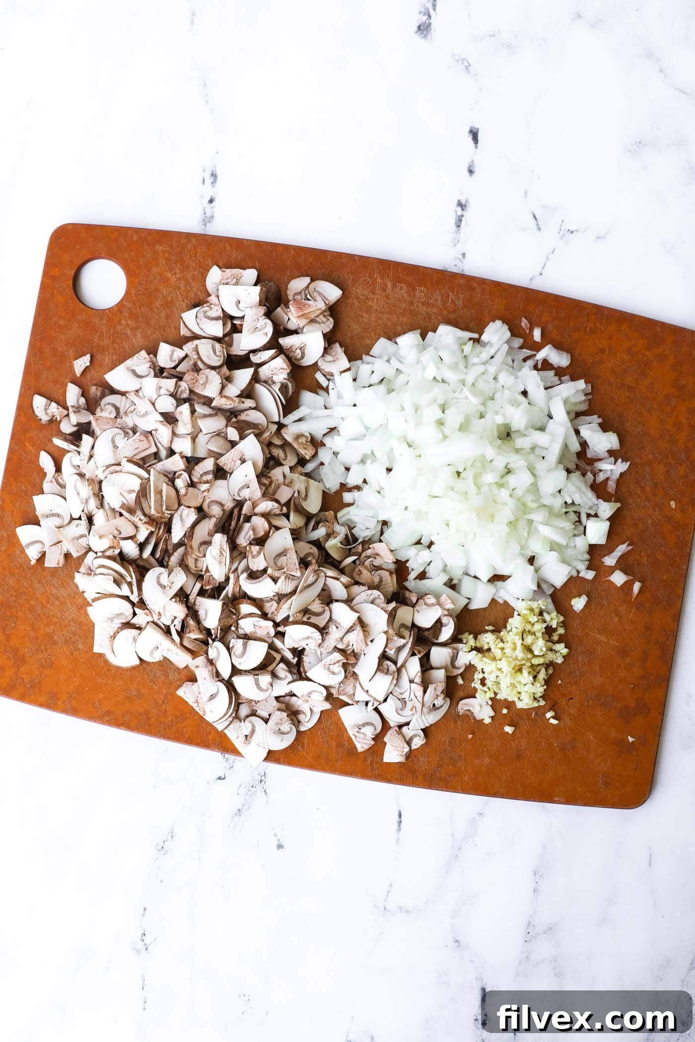 Diced garlic, chopped onion, and sliced mushrooms neatly arranged on a cutting board, prepped for the creamy beef and mushroom skillet.