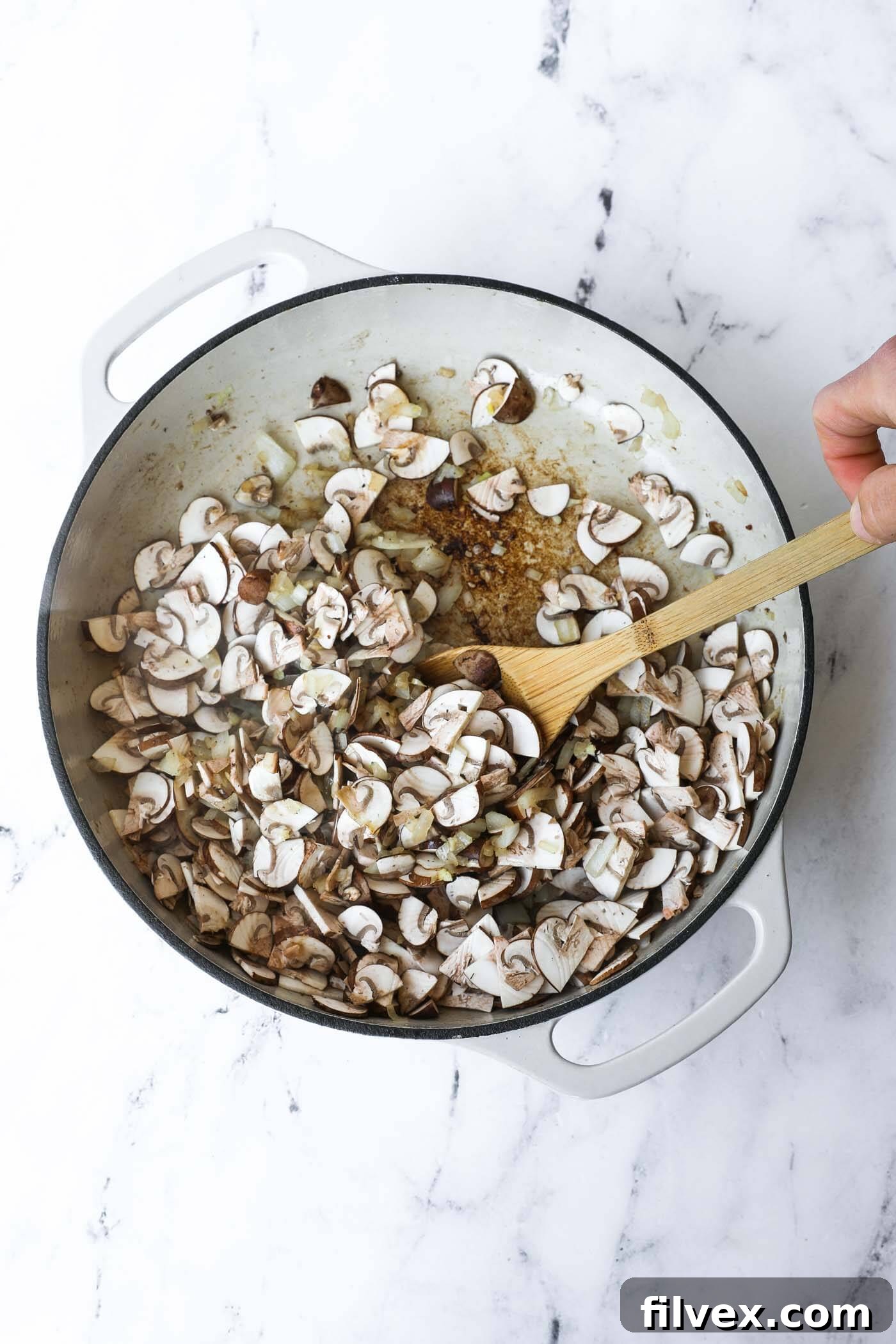 Sliced mushrooms added to the skillet with cooked onions and garlic, sautéing to soften and release their moisture.