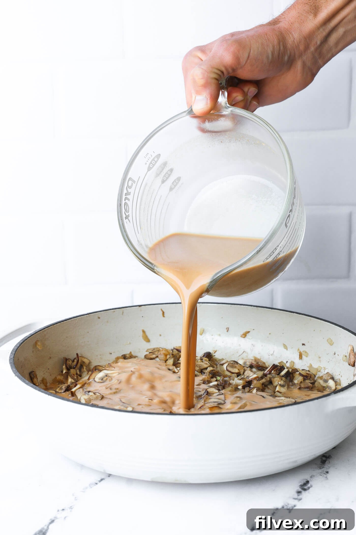 The whisked creamy sauce being poured into the skillet with sautéed vegetables, beginning the process of thickening.