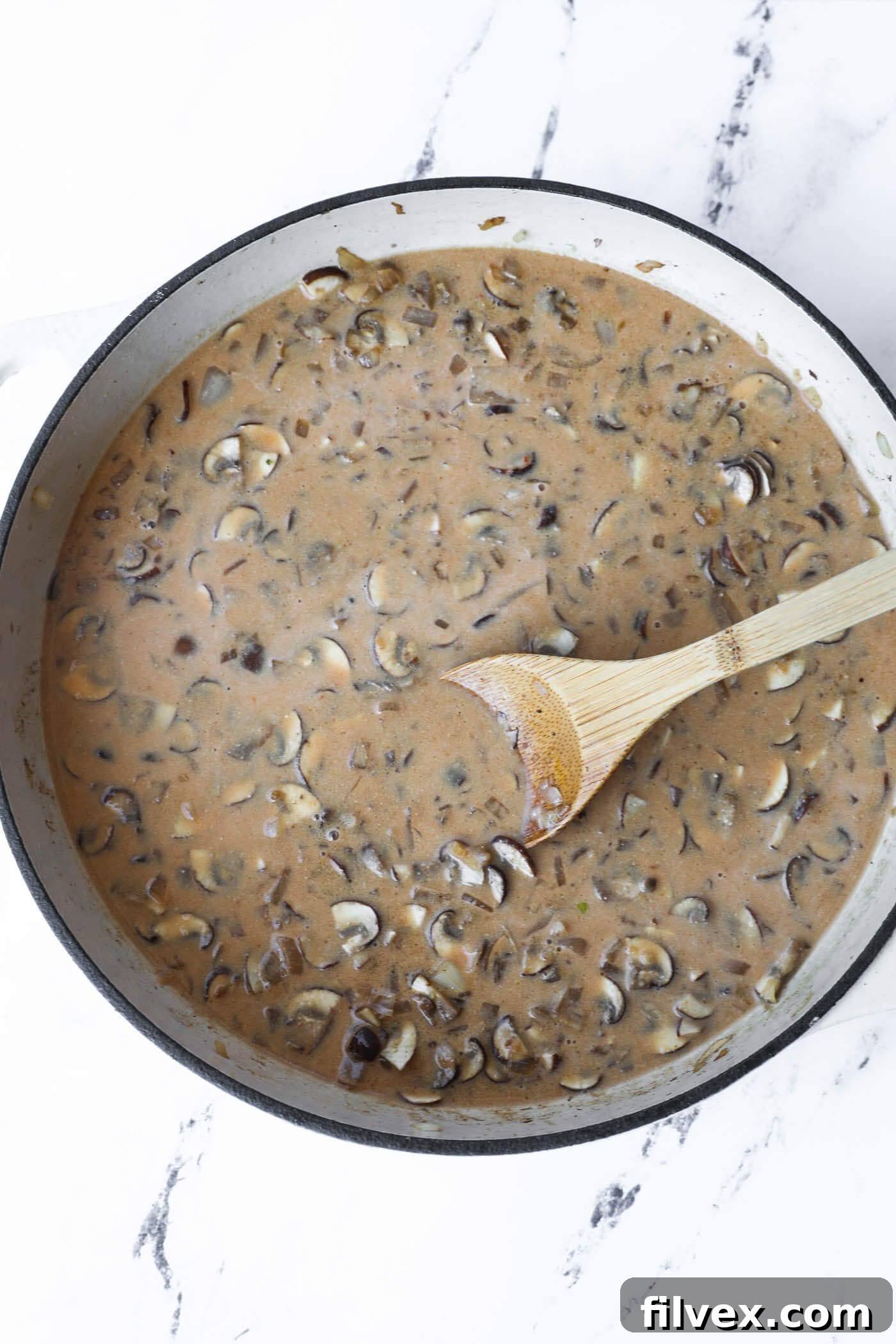 The creamy mushroom sauce simmering in the skillet, visibly thickening into a rich gravy-like consistency.