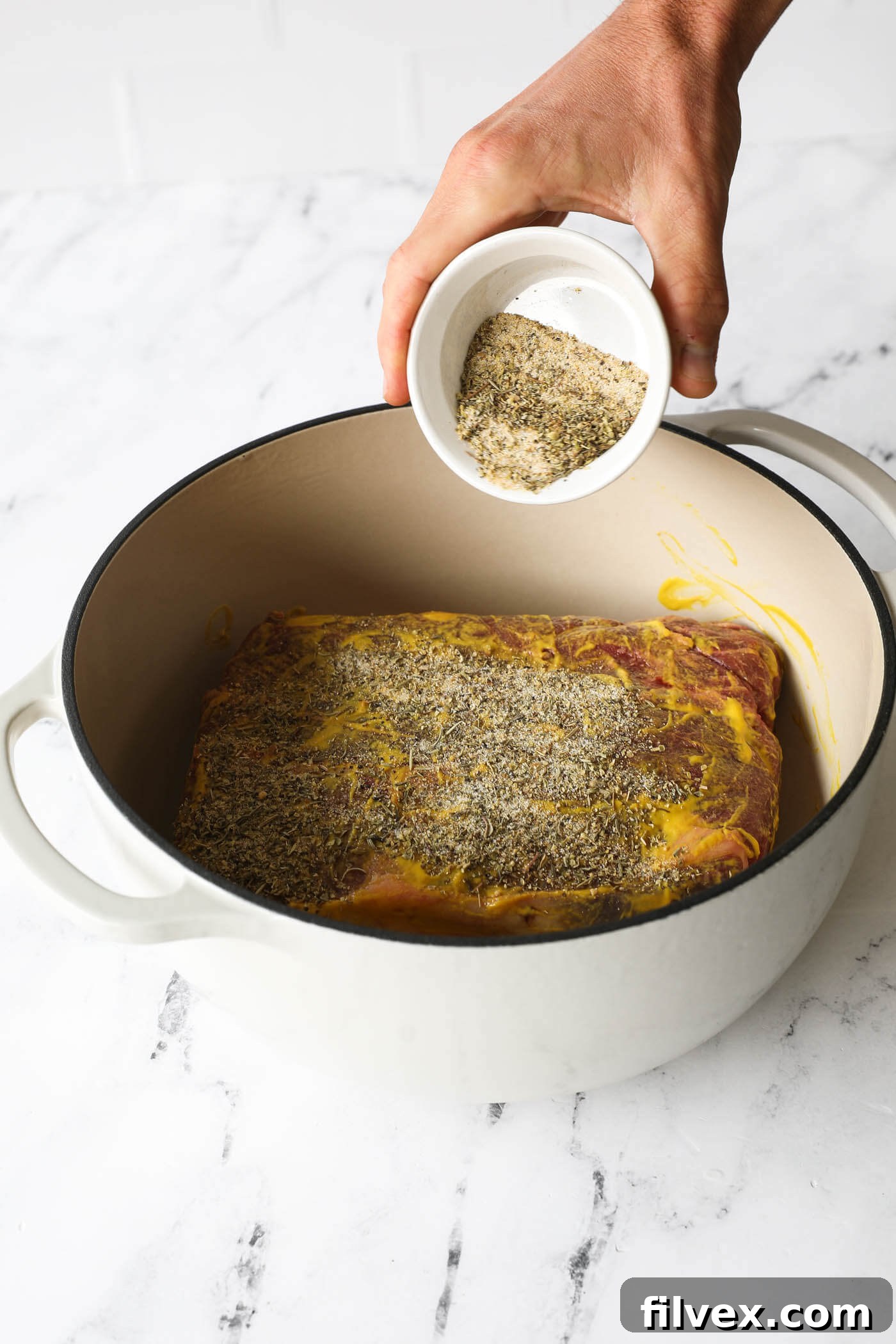 Coating the mustard-covered pot roast with homemade seasoning