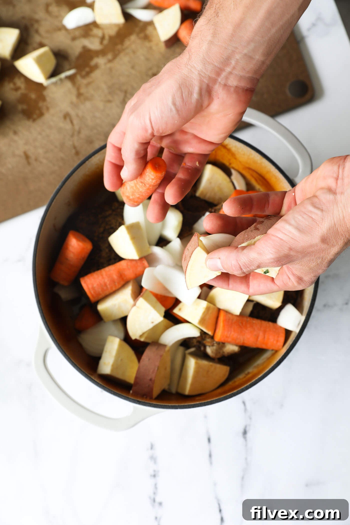 Adding prepared vegetables to the Dutch oven with the partially cooked pot roast