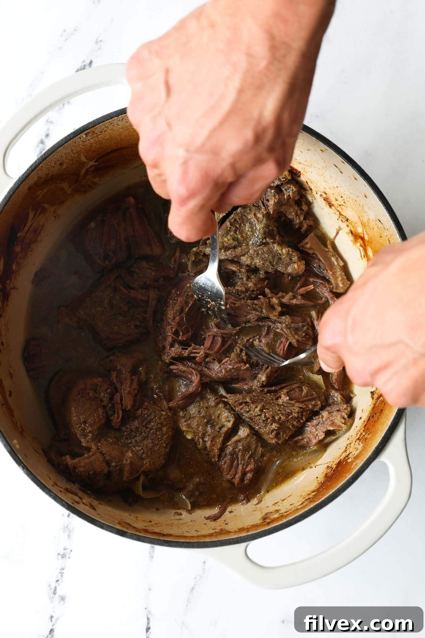 Shredding tender pot roast with two forks in the Dutch oven