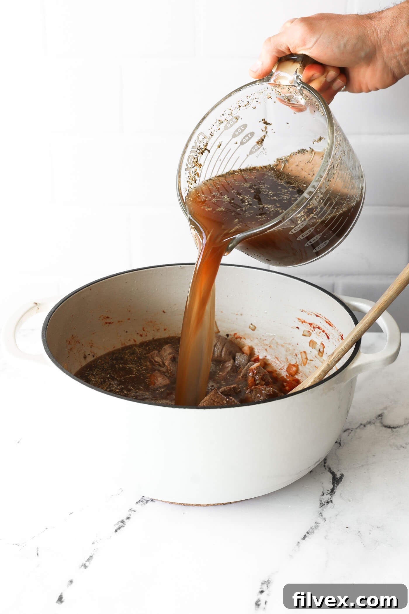 Pouring the stew broth mixture into the Dutch oven with the beef and deglazing the pot.