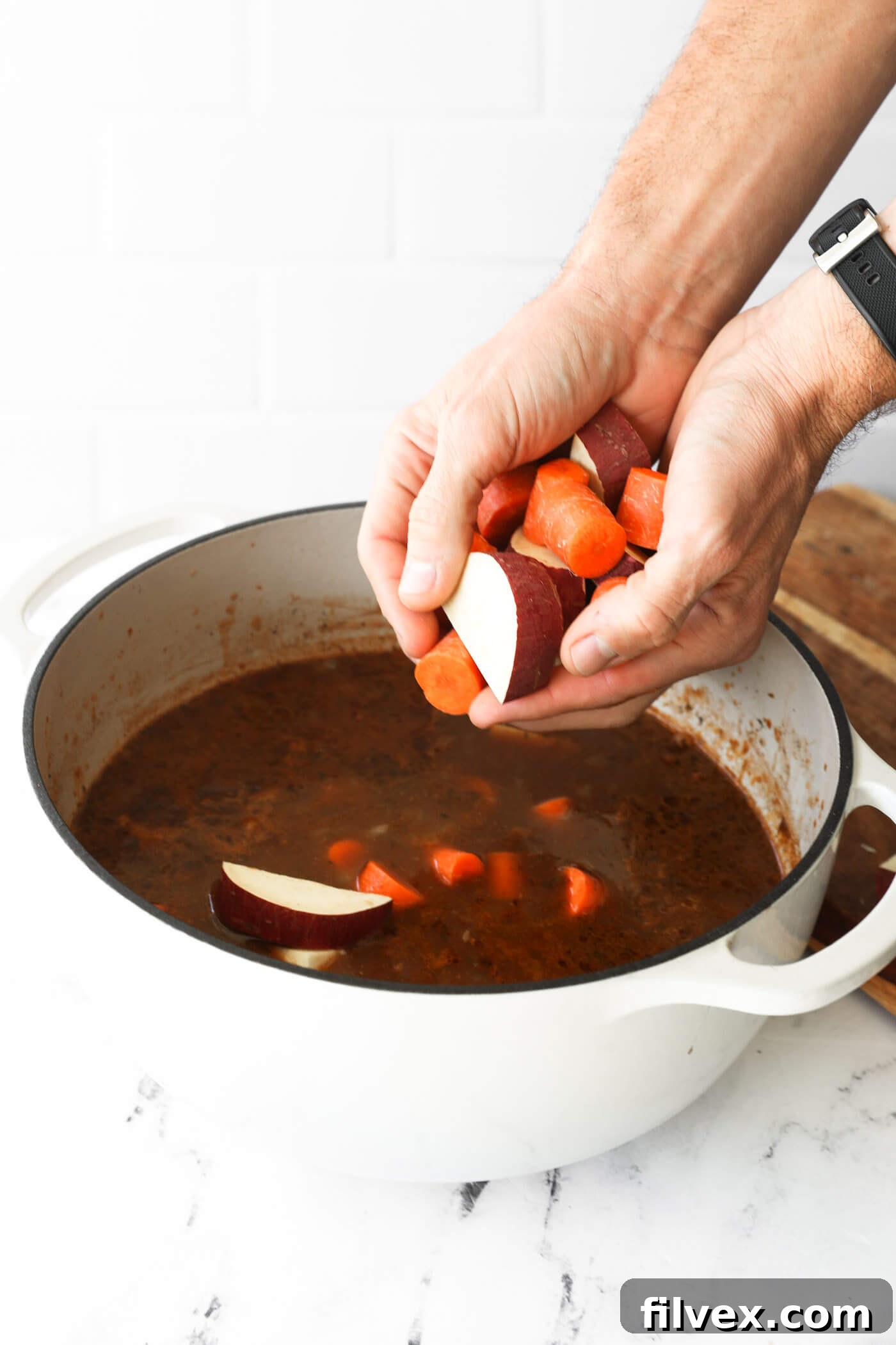 Adding carrots and potatoes to the simmering beef stew after 2 hours of baking.