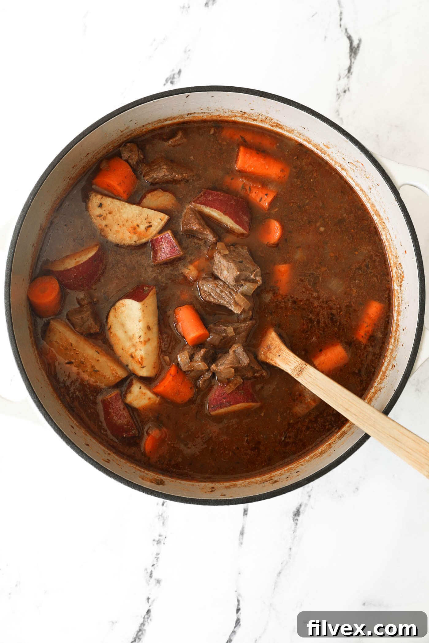 Returning the covered Dutch oven to the oven to finish baking until vegetables are tender.